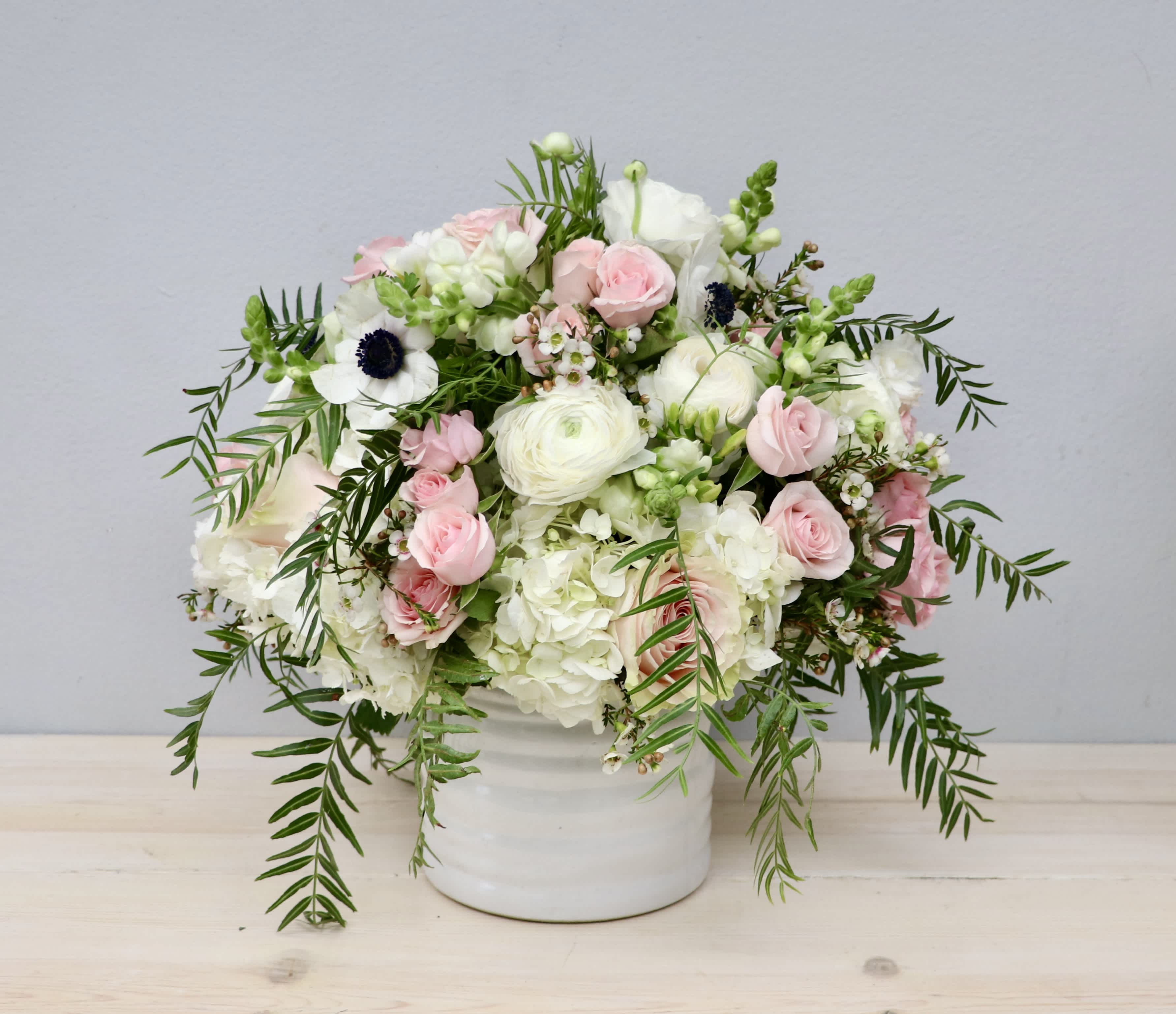 White and blush flower arrangement with trailing greenery in a white ceramic vase.