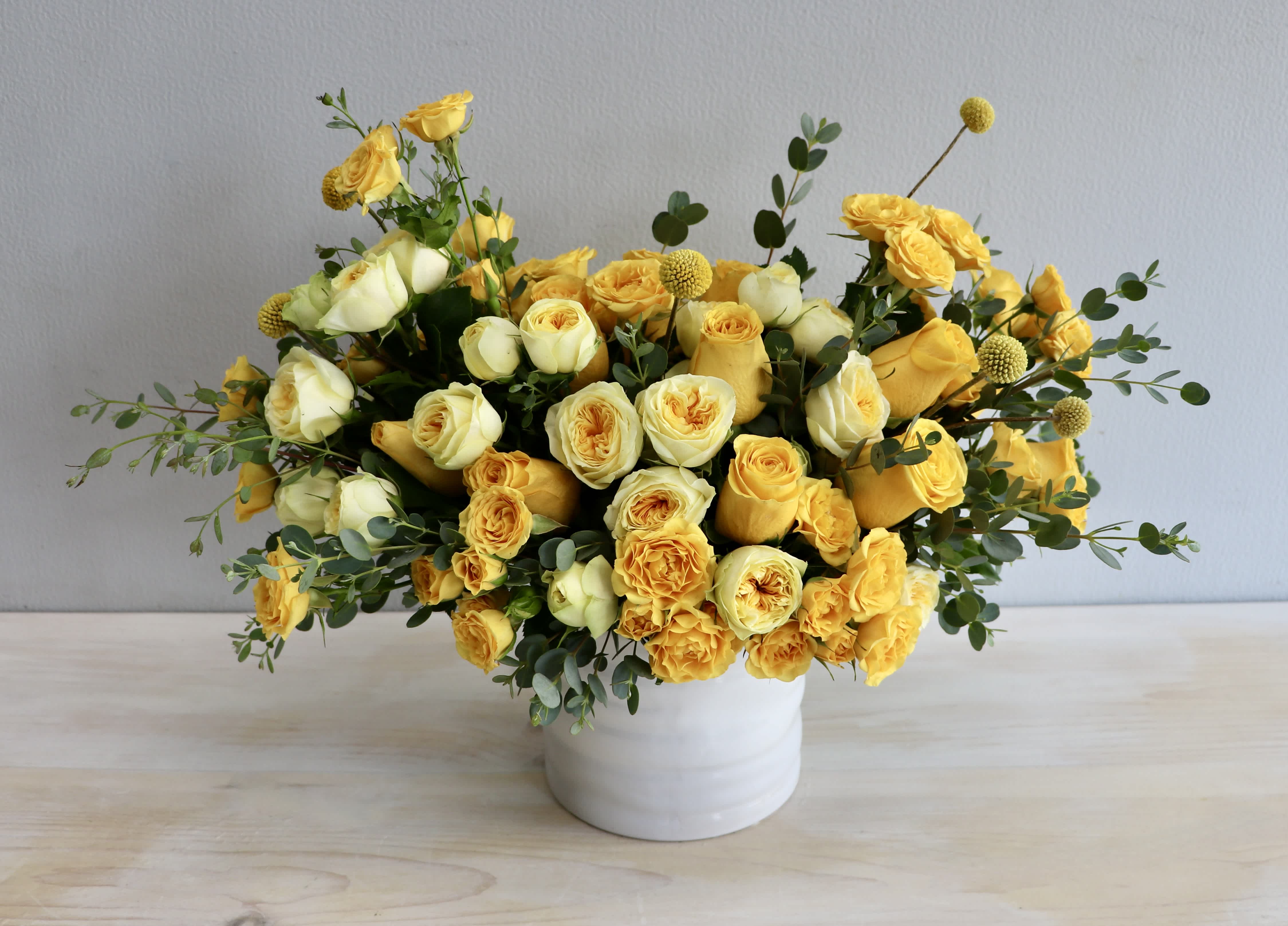 Low arrangement of yellow and cream roses in a white ceramic vase