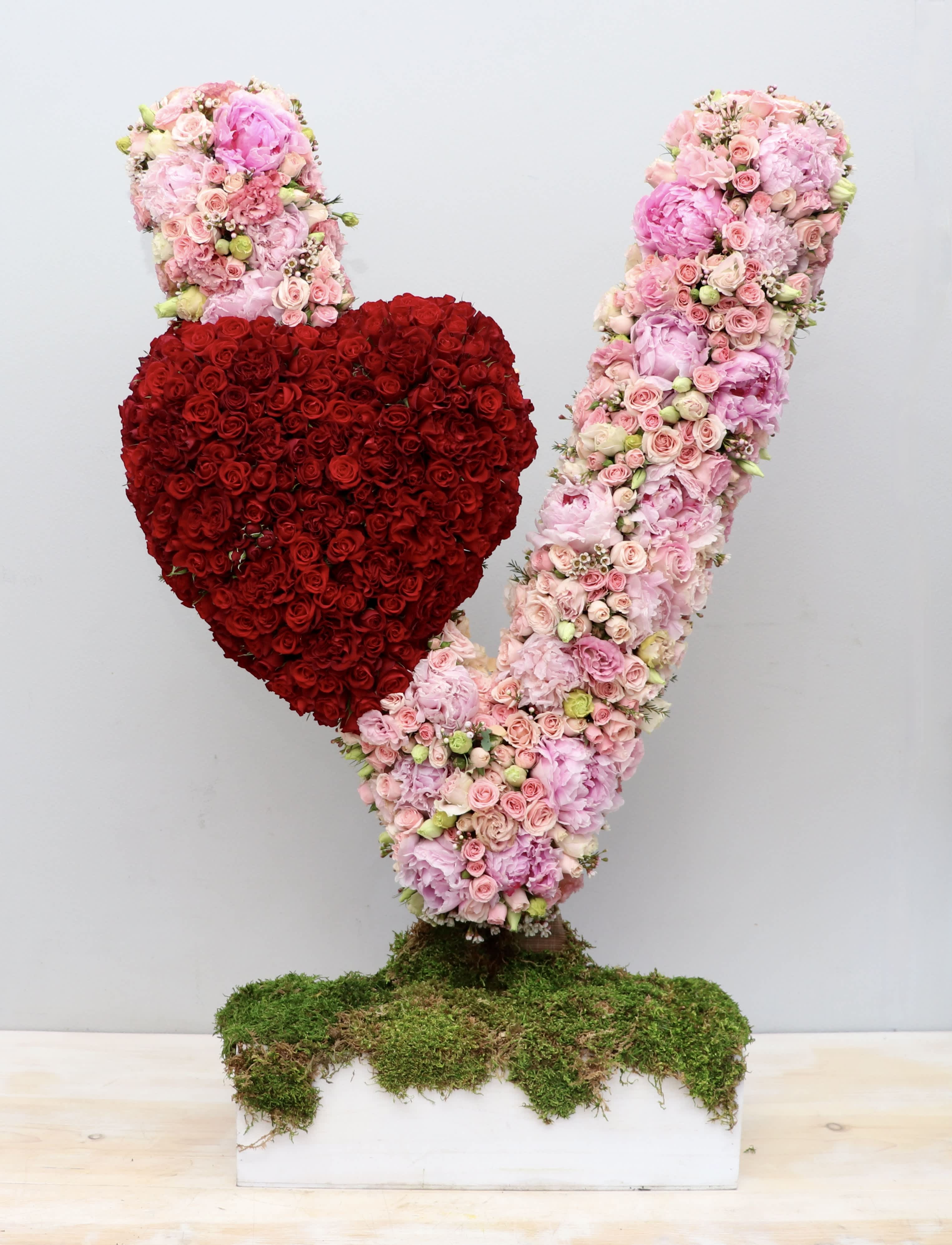 Tall pink floral V sculpture with a red rose heart on a moss-covered rectangular base