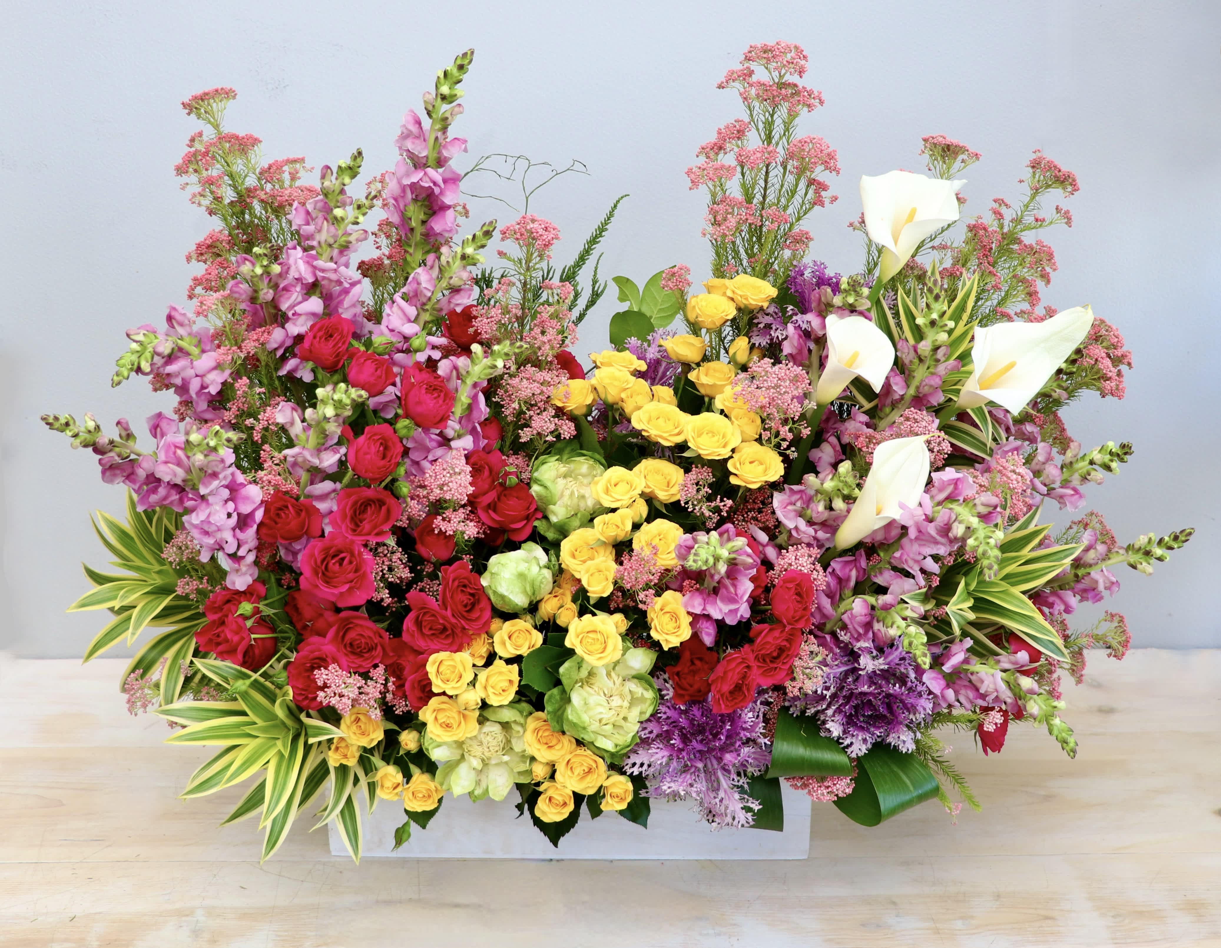 Large rectangular arrangement of bright pink, yellow, red, and white flowers in a white container