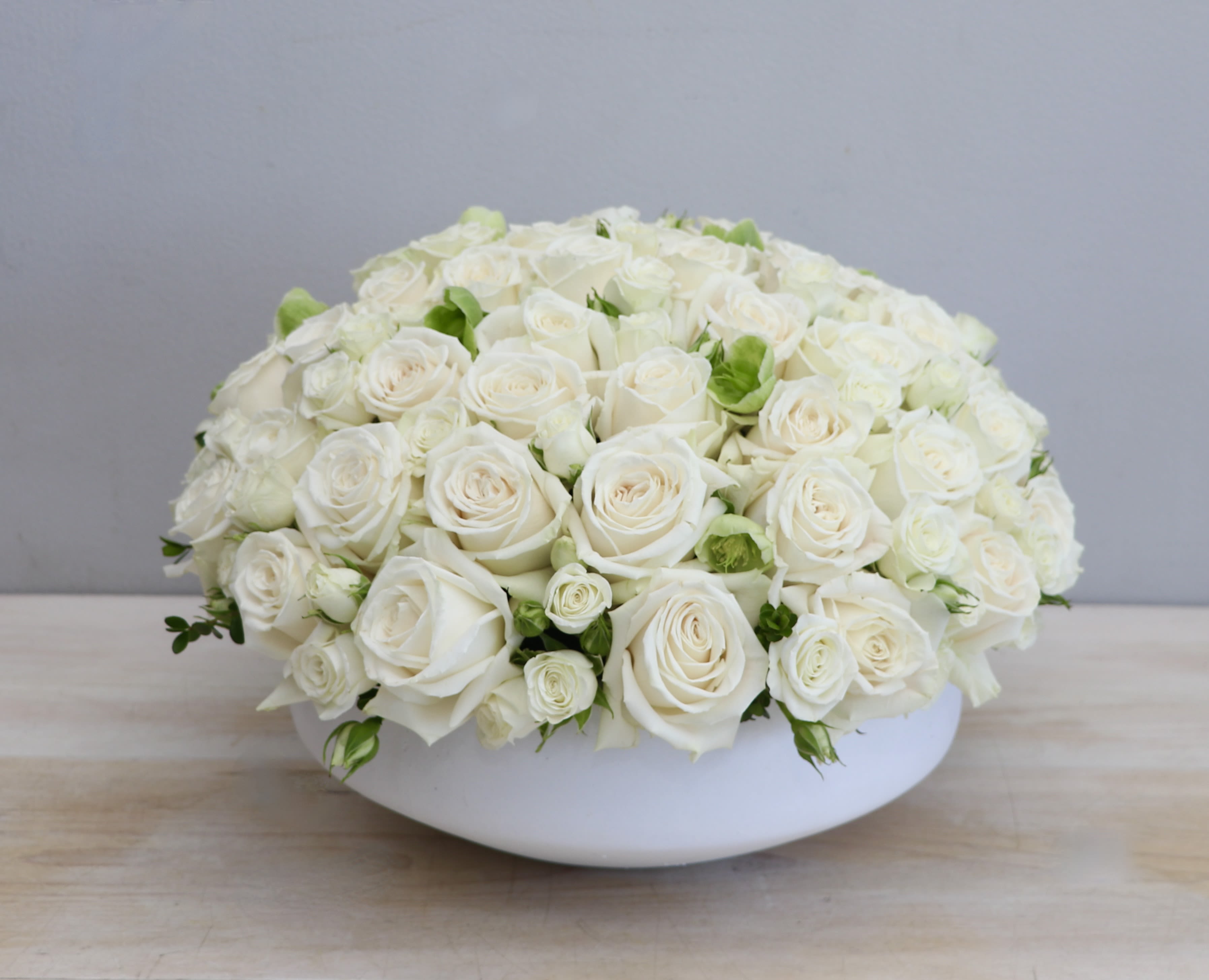 Low dome arrangement of cream white roses tightly packed in a round white bowl