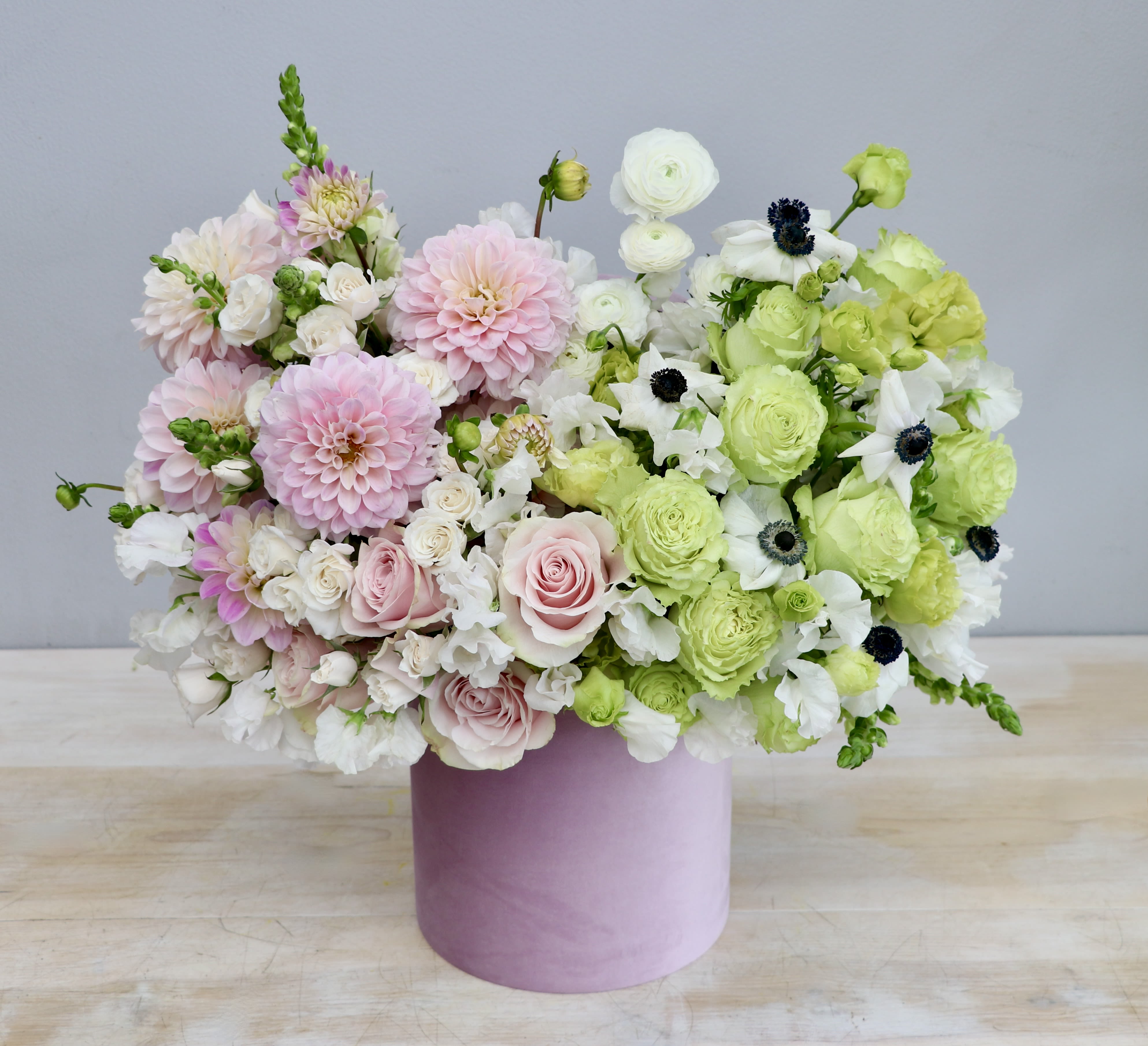 Round pastel arrangement of pink and green flowers in a pink hatbox-style container