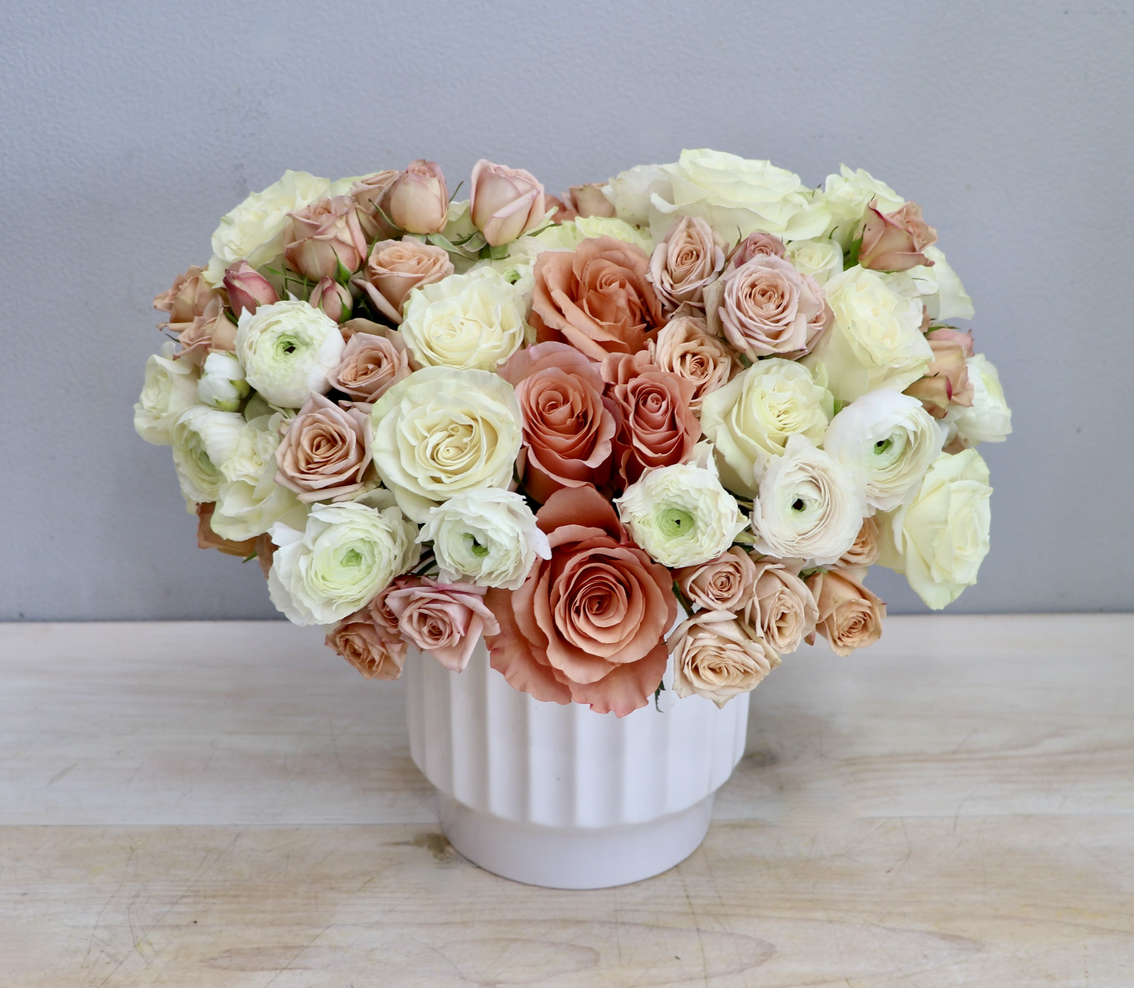 Low arrangement of peach and cream roses with ranunculus in a white ceramic vase