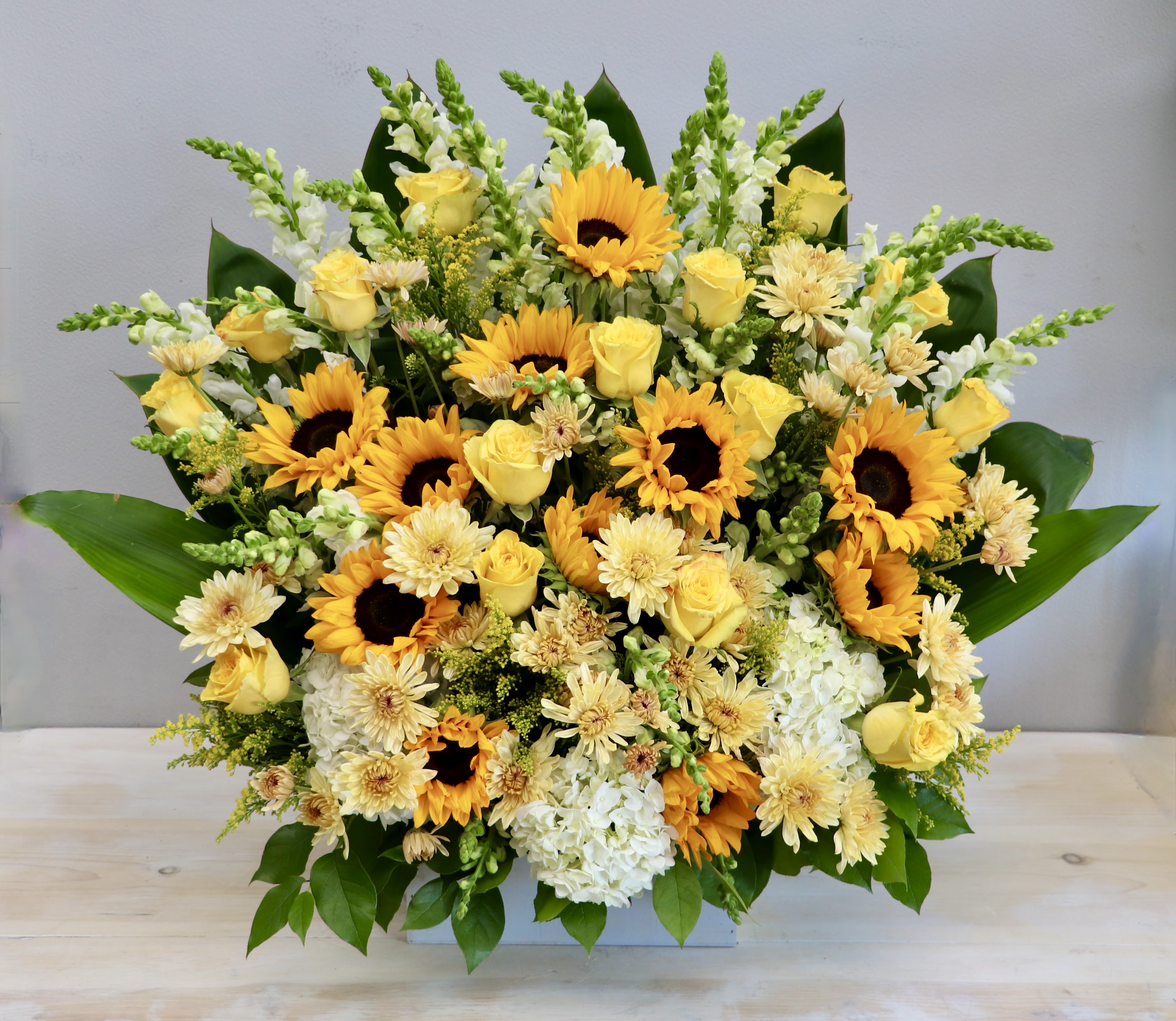 Large arrangement of yellow sunflowers, roses, and white blooms in a low white container
