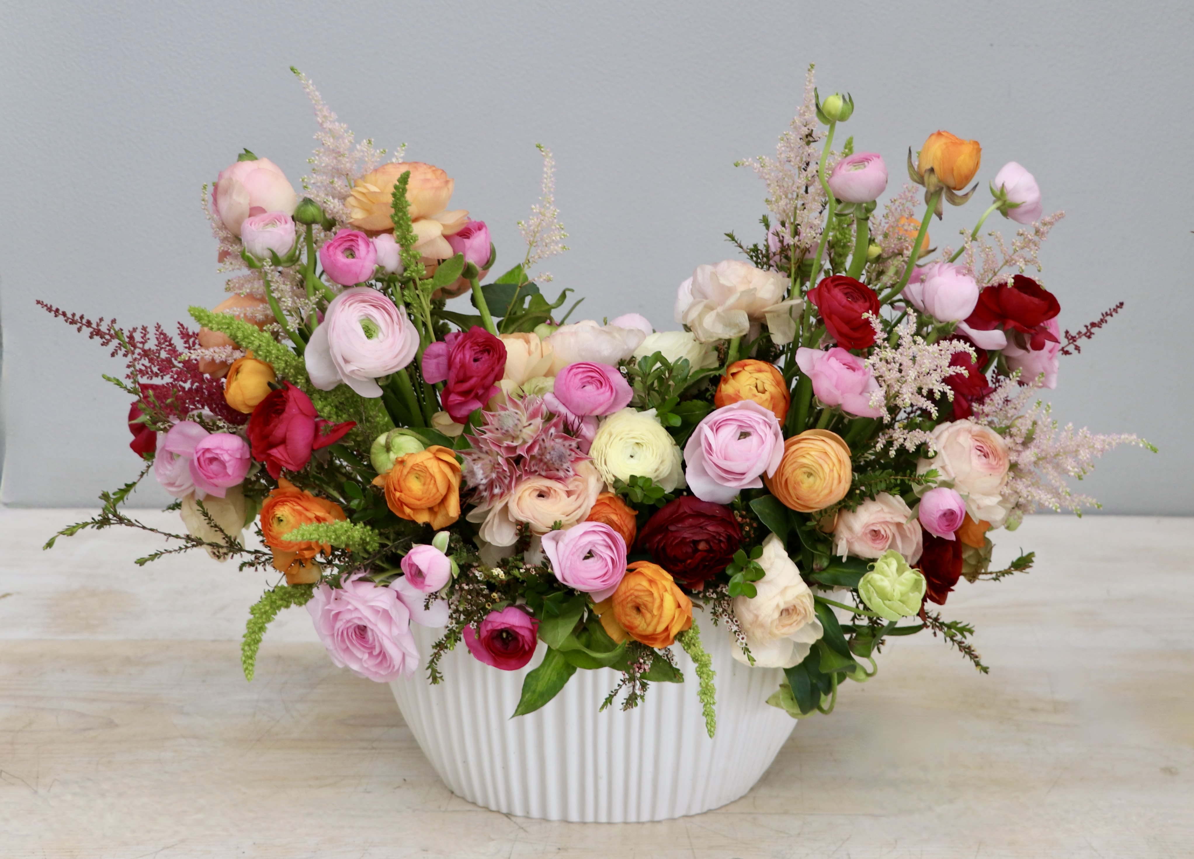 Low white ceramic bowl filled with pink, red, orange, and cream ranunculus arrangement