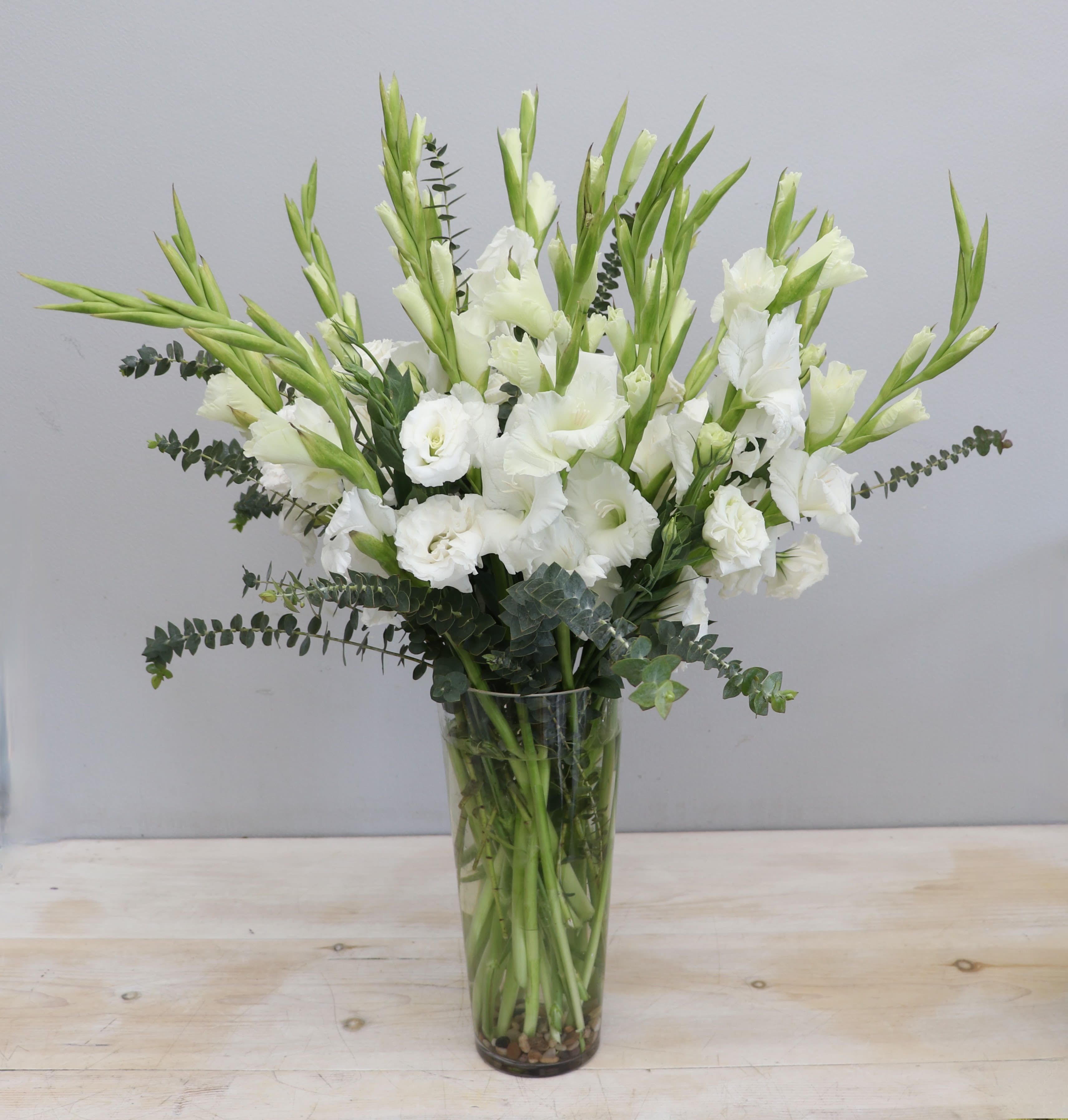 Tall arrangement of white gladiolus and lisianthus in a clear glass vase