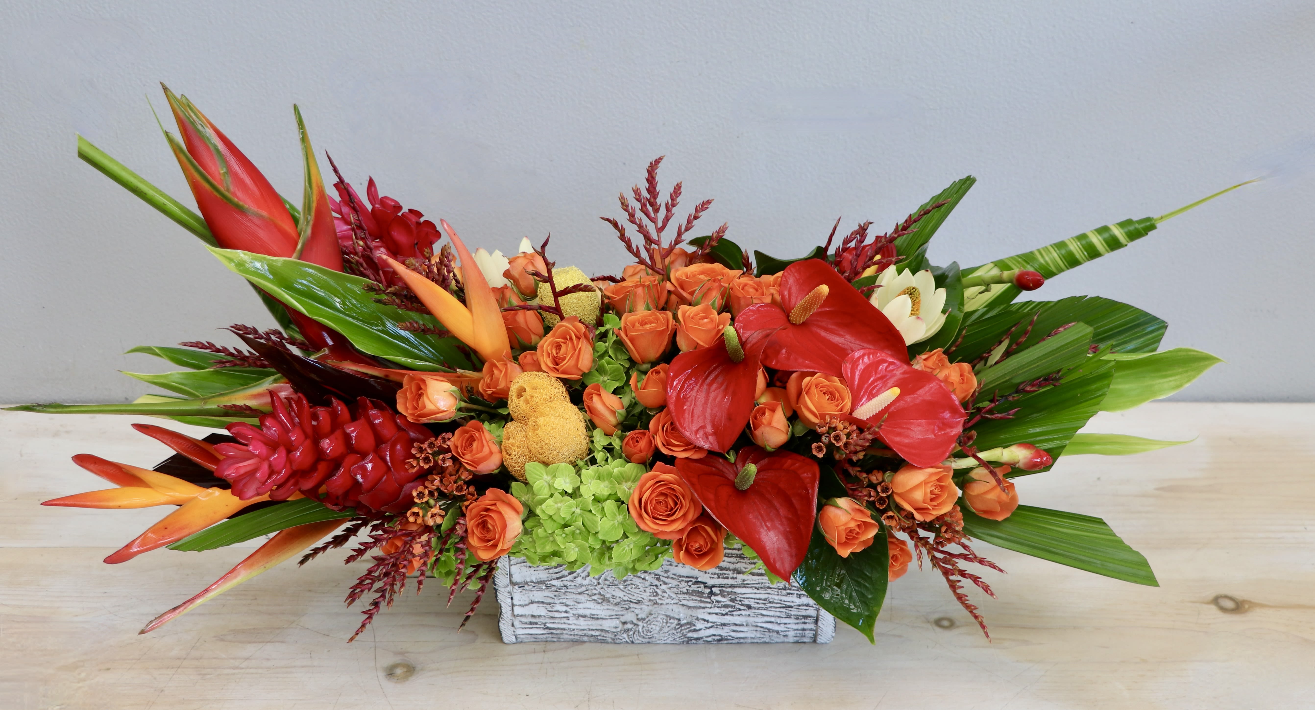Low tropical centerpiece with orange roses, red anthuriums, and green hydrangeas in a white wooden box