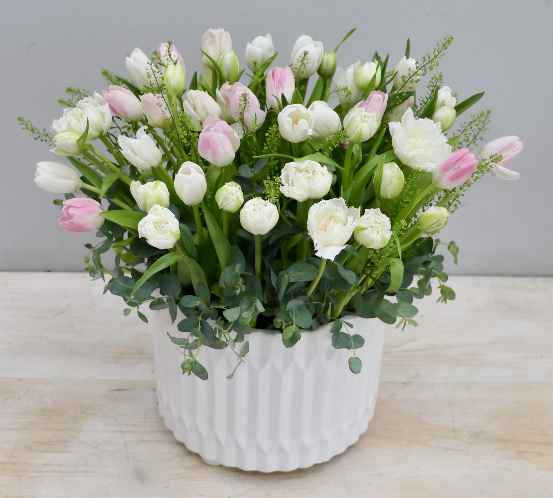 White and pale pink tulips in a white textured ceramic pot with lush foliage