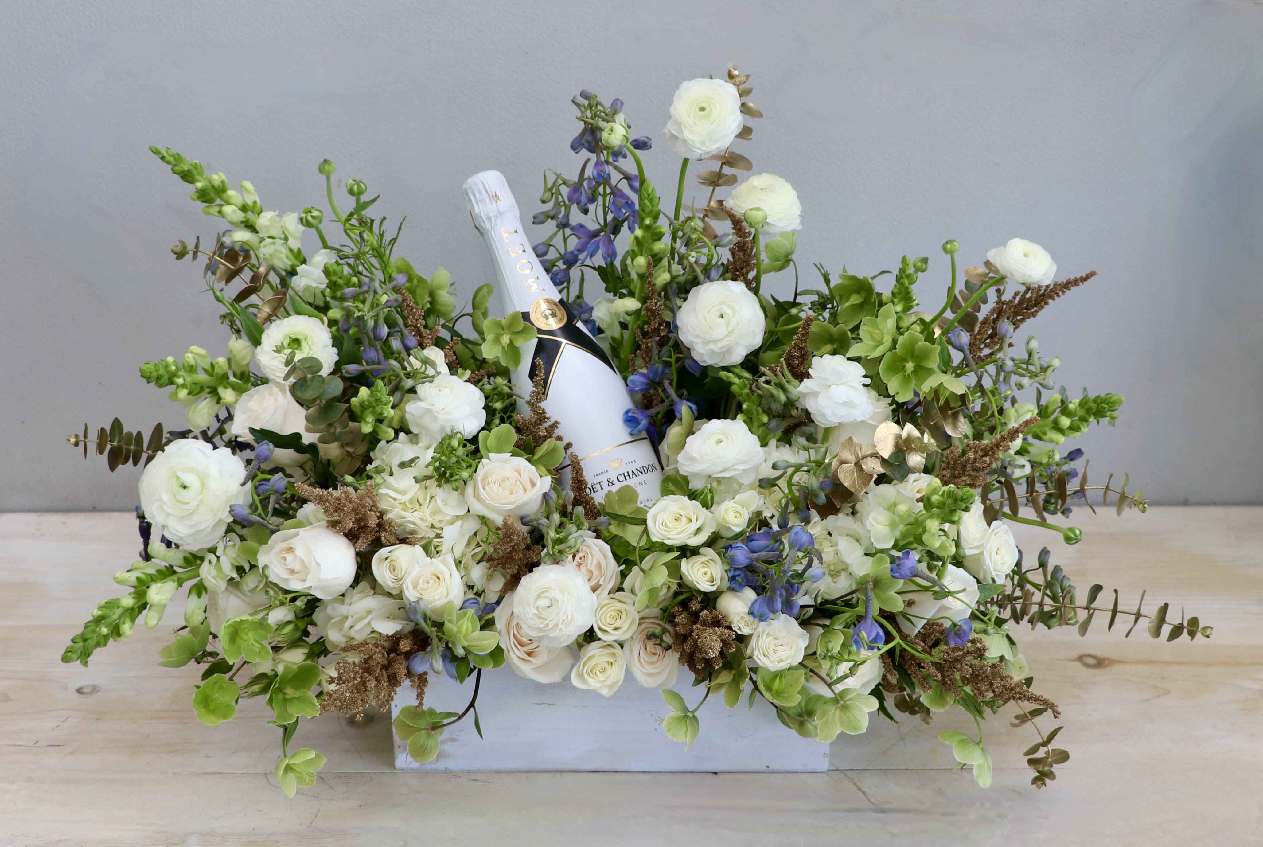 Low white box arrangement of white and green flowers with a champagne bottle nestled in the center