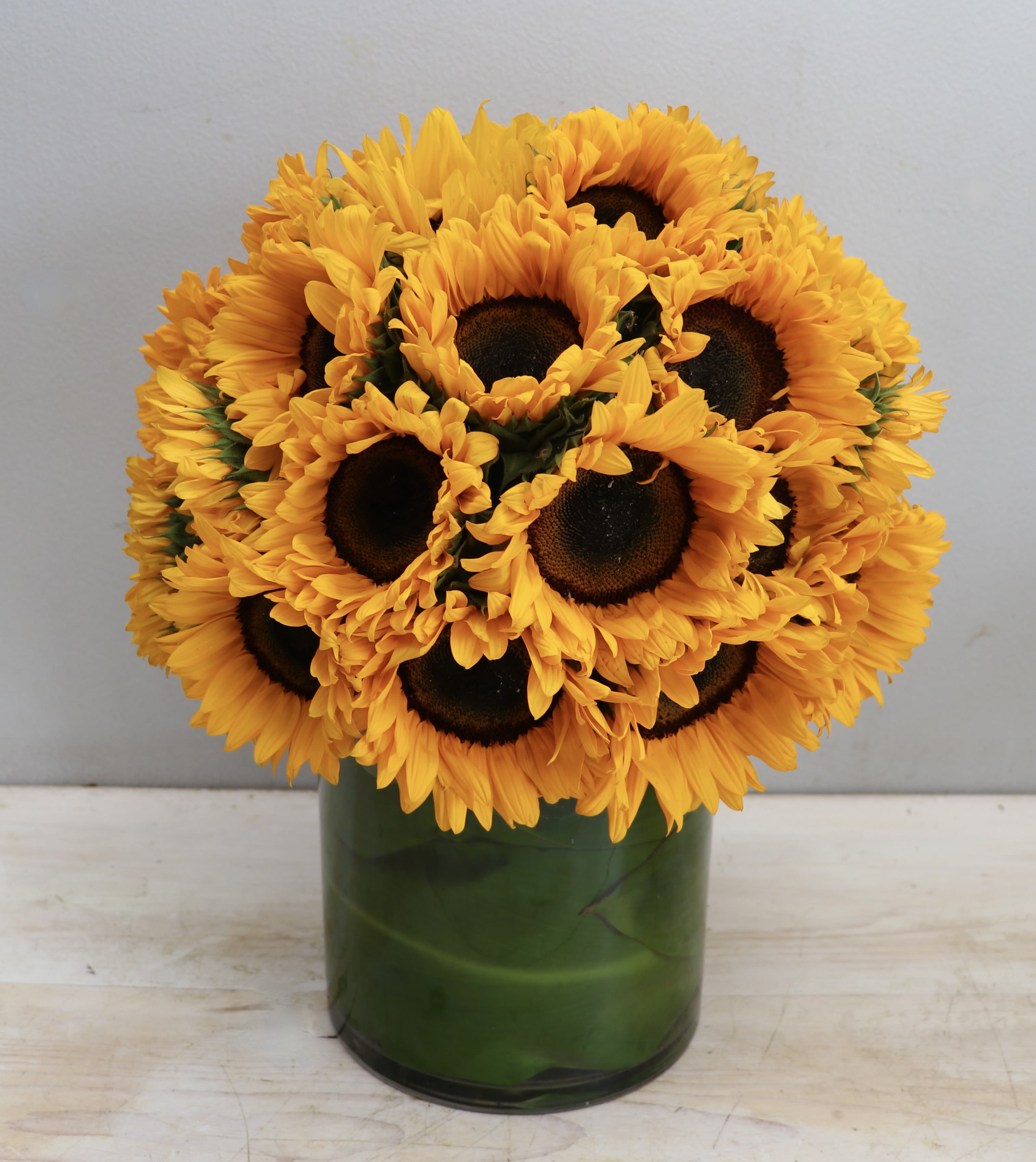 Compact arrangement of bright yellow sunflowers tightly clustered in a clear glass cylinder vase