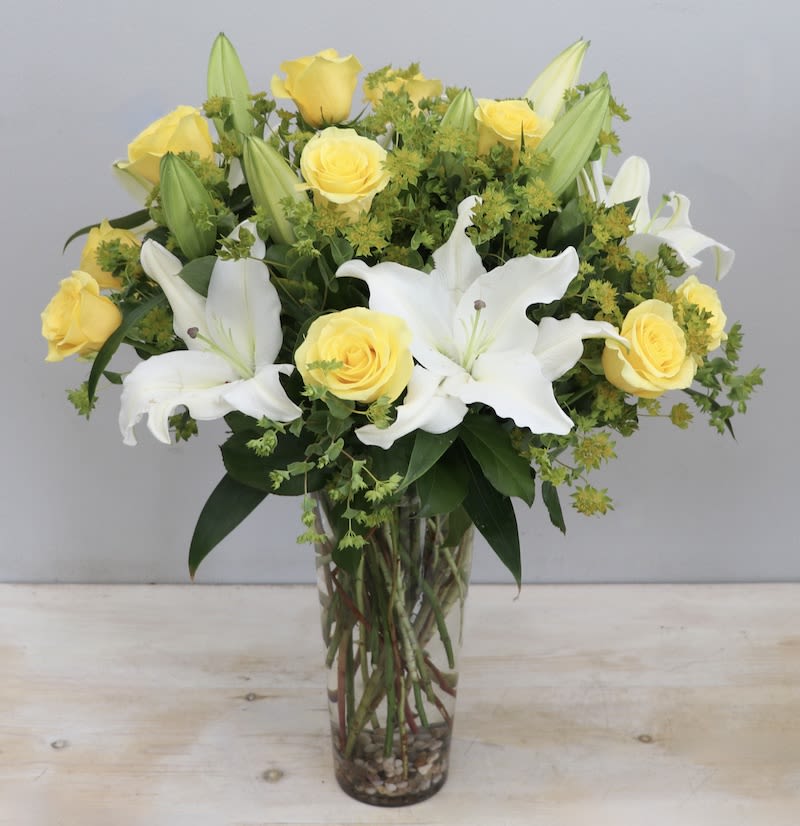 Tall glass vase of yellow roses and white lilies with green filler flowers