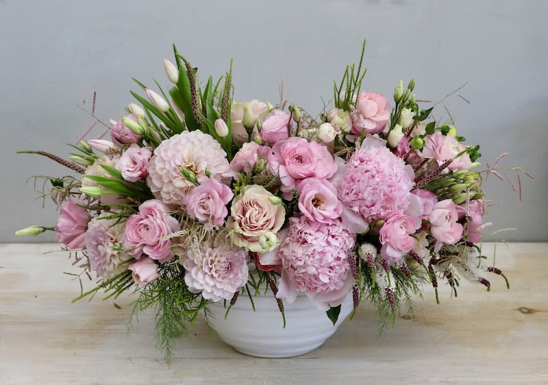 Low pink arrangement of roses, peonies, and other blooms in a white ceramic bowl
