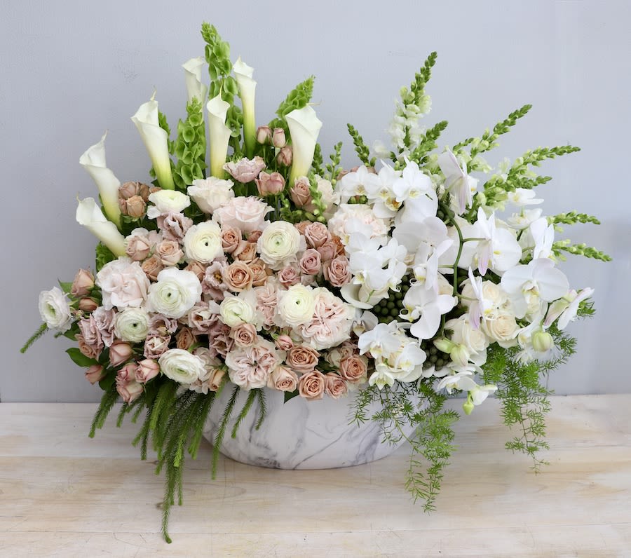 Low marble container filled with blush roses, white ranunculus, calla lilies, and cascading white orchids