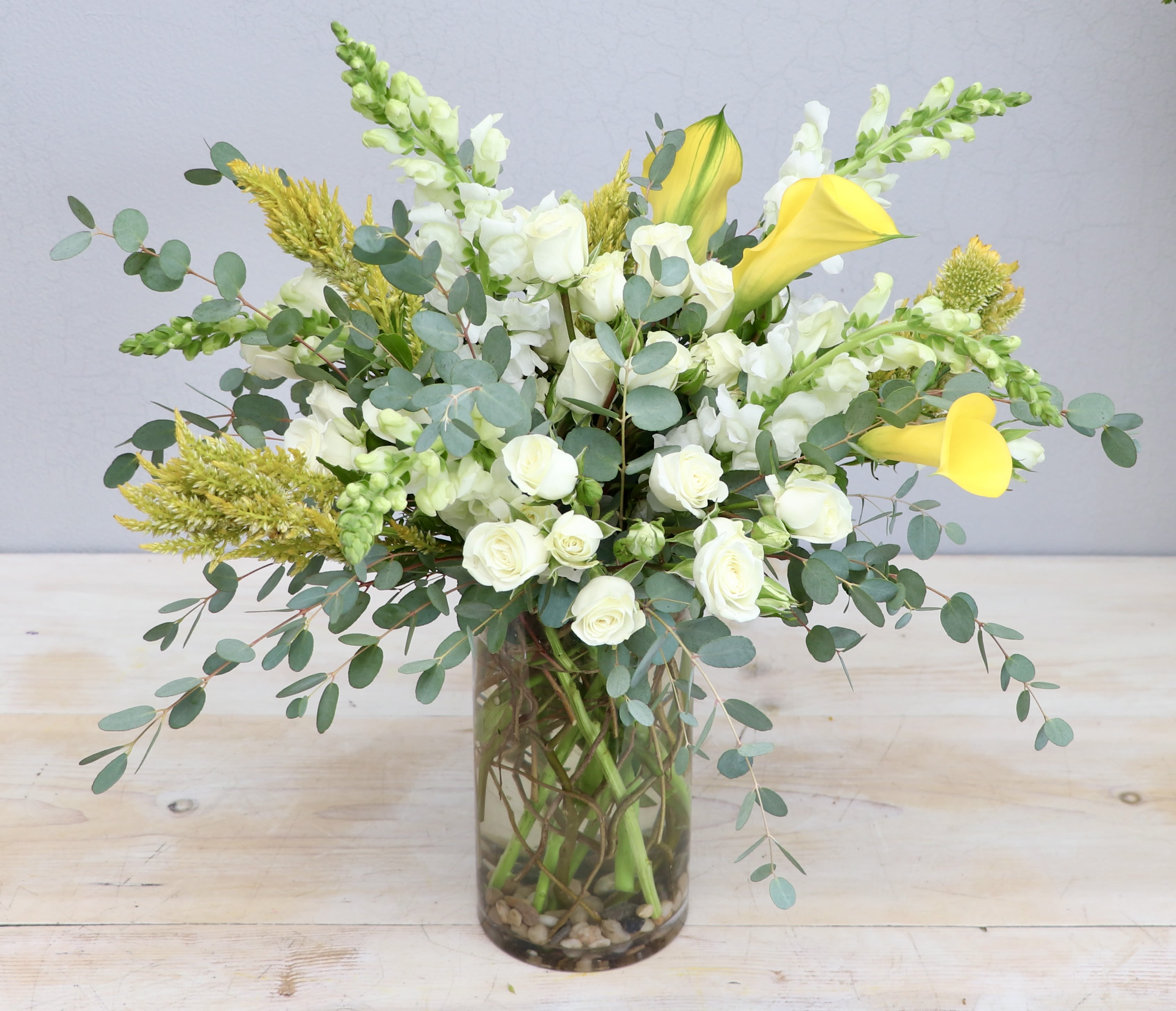 Tall arrangement of white roses, white snapdragons, and yellow calla lilies in a clear glass vase