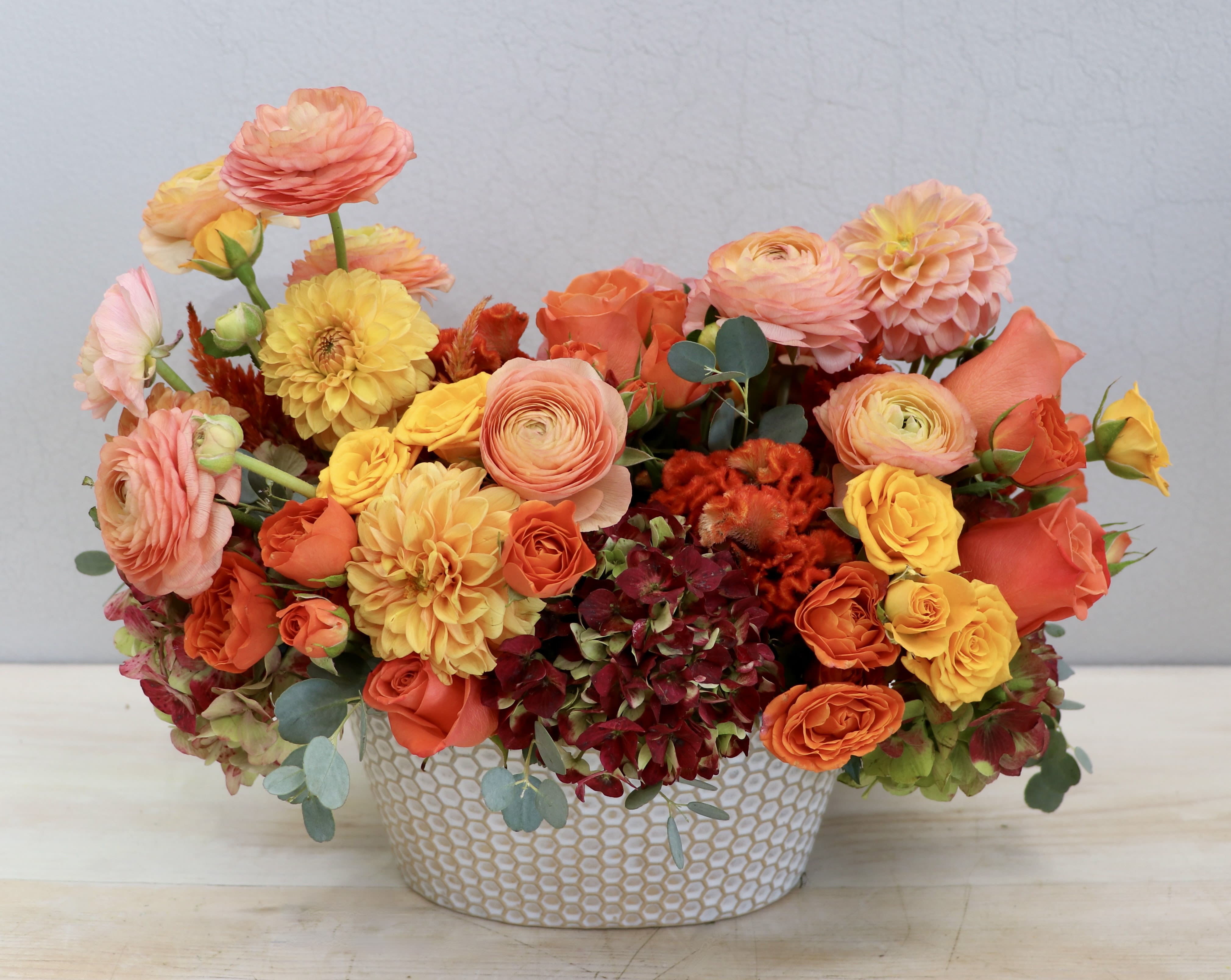 Low arrangement of orange, yellow, and peach flowers in a white patterned ceramic container