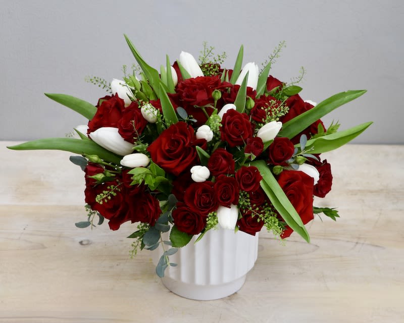 Low red rose and white tulip arrangement in a white ceramic vase