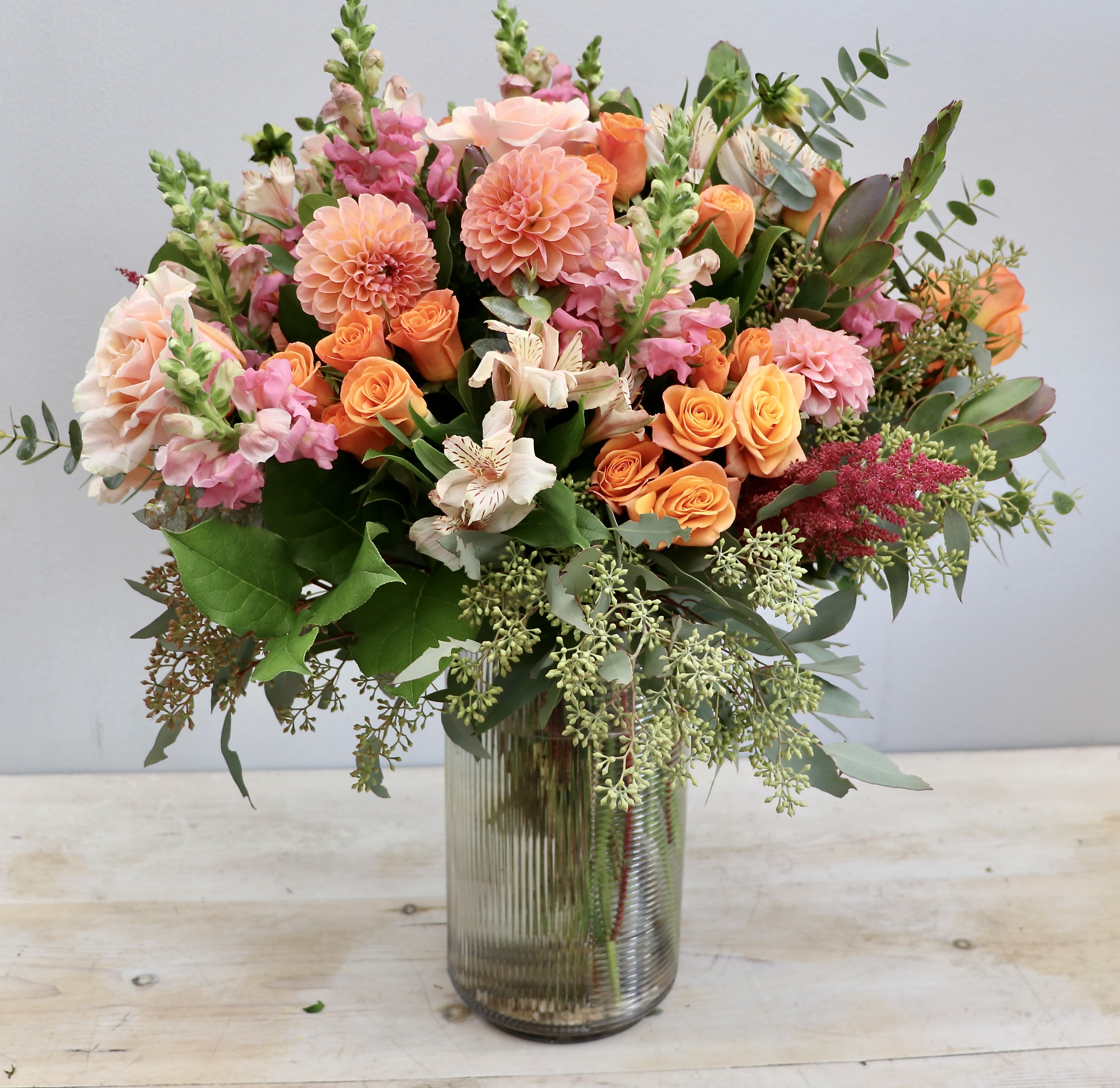 Tall mixed bouquet of pink and orange flowers in a ribbed glass vase