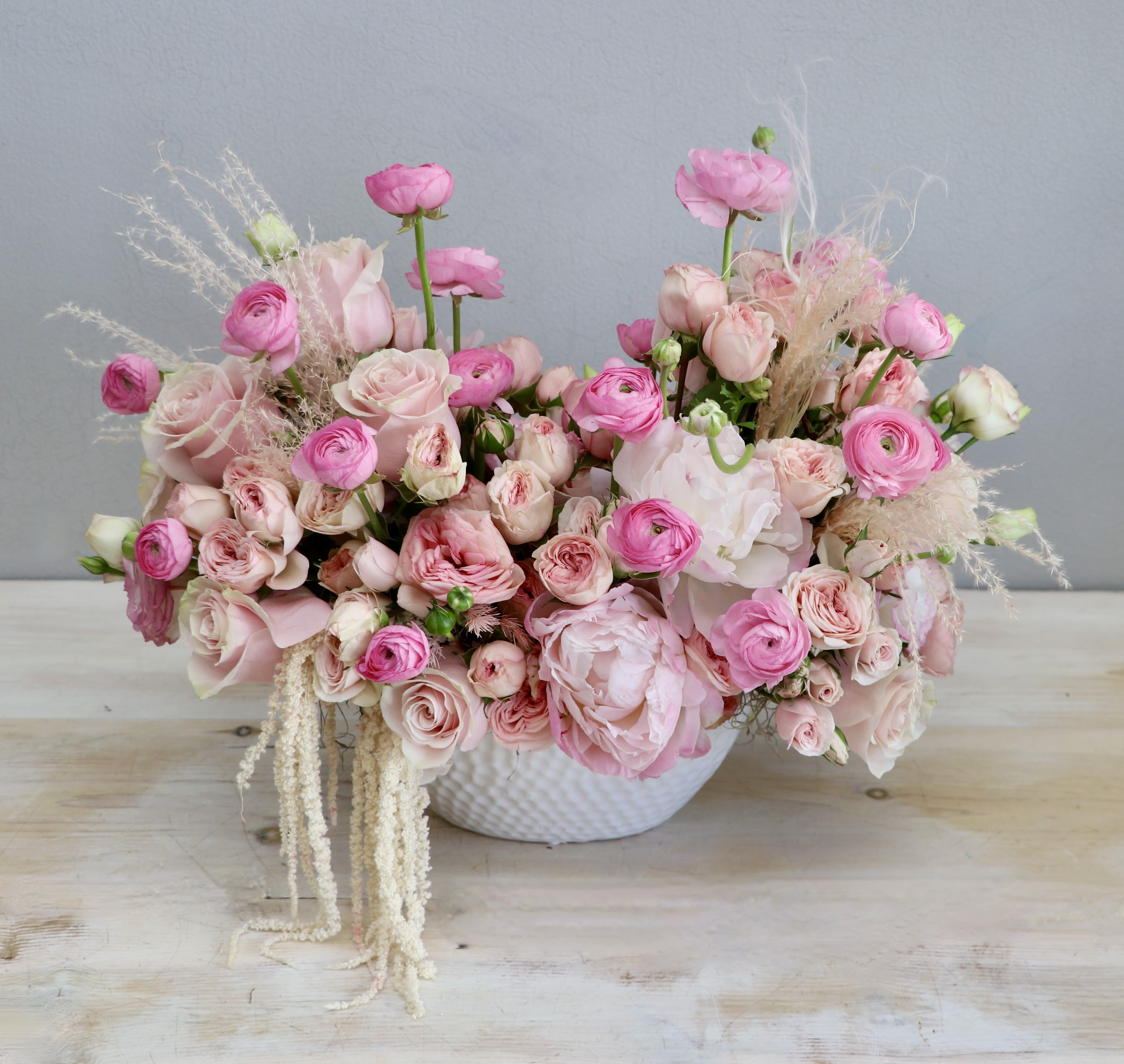 Low bowl arrangement of pink roses, ranunculus, and peonies in a white ceramic container