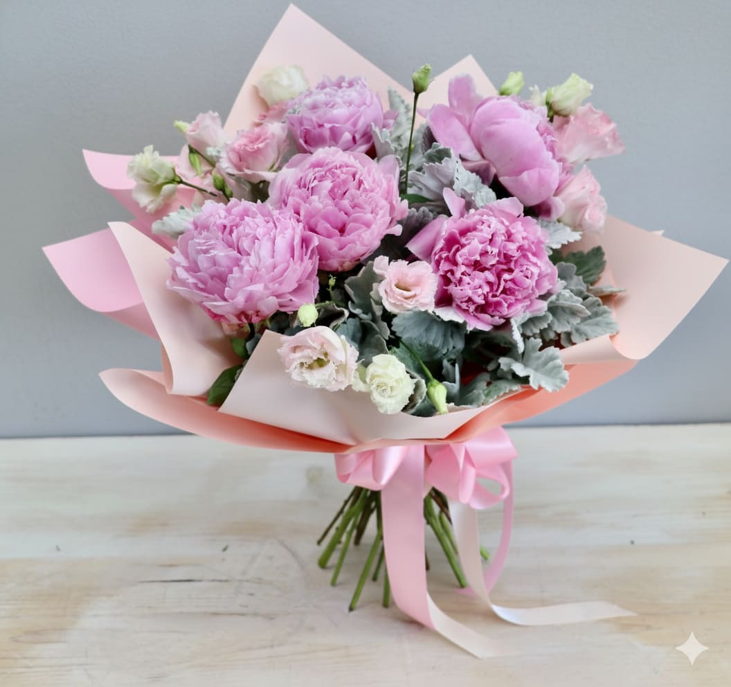 Hand-tied bouquet of pink peonies and pale lisianthus wrapped in pink paper with a satin ribbon