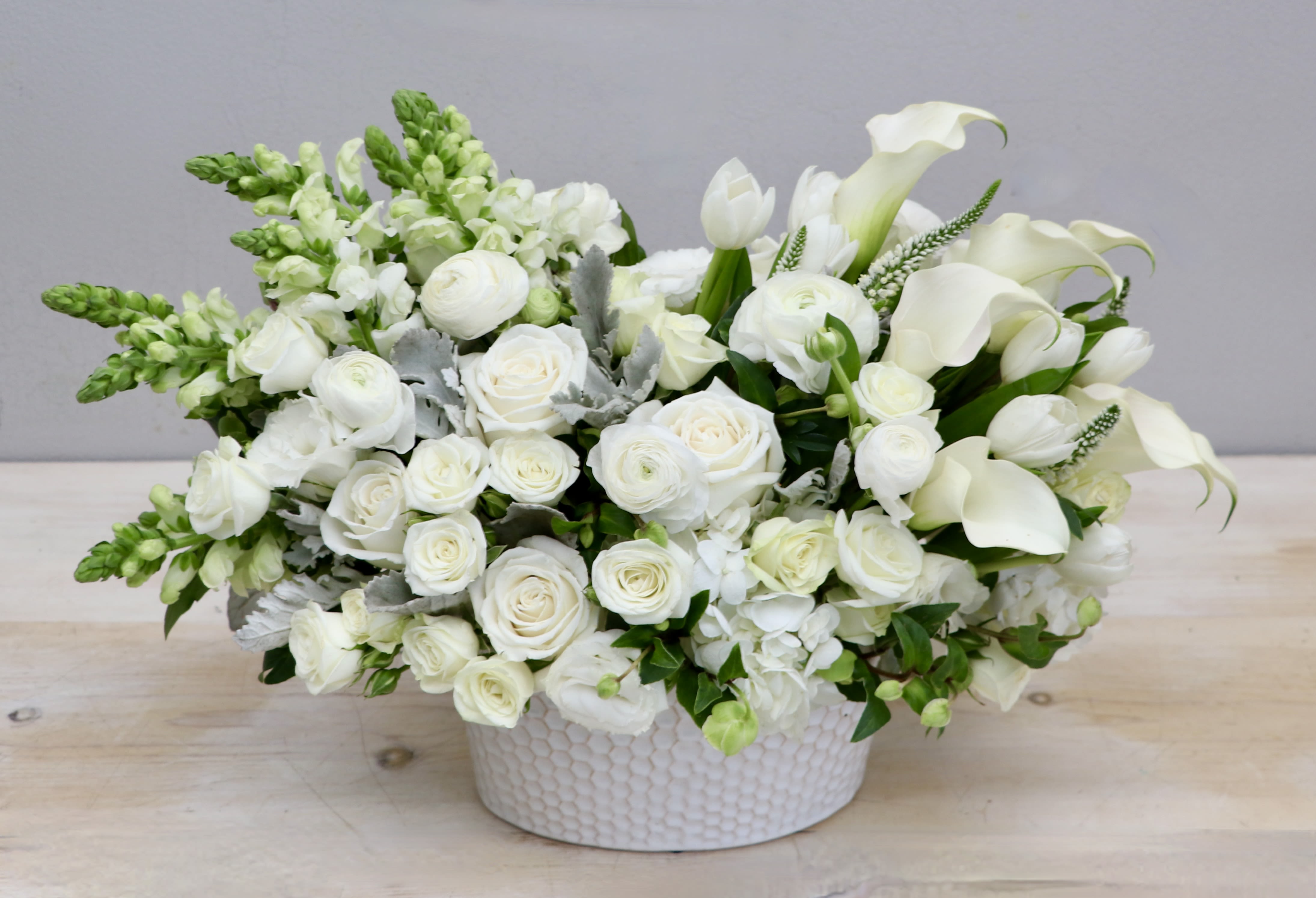 Low white arrangement of roses, calla lilies, tulips, and snapdragons in a round ceramic bowl