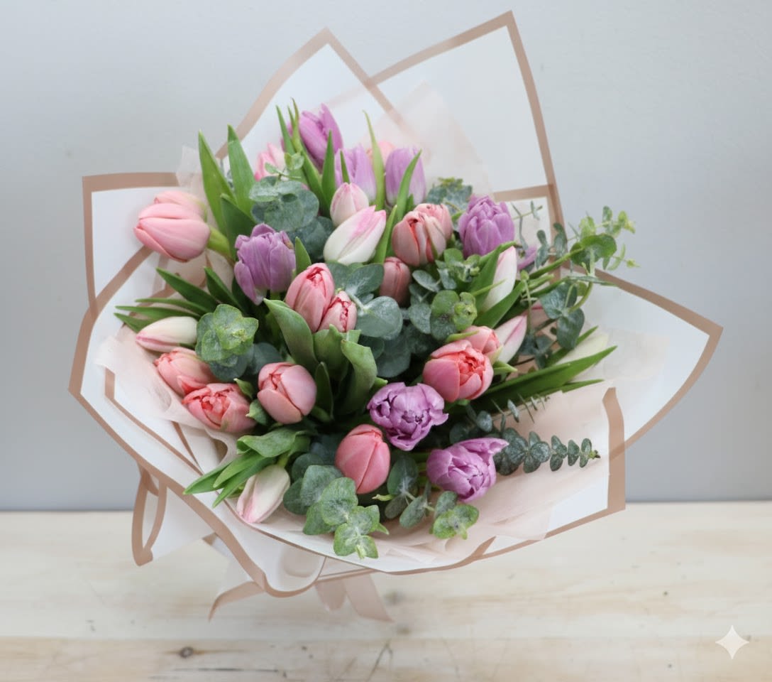 Hand-tied bouquet of pink and purple tulips with eucalyptus wrapped in white and beige paper.
