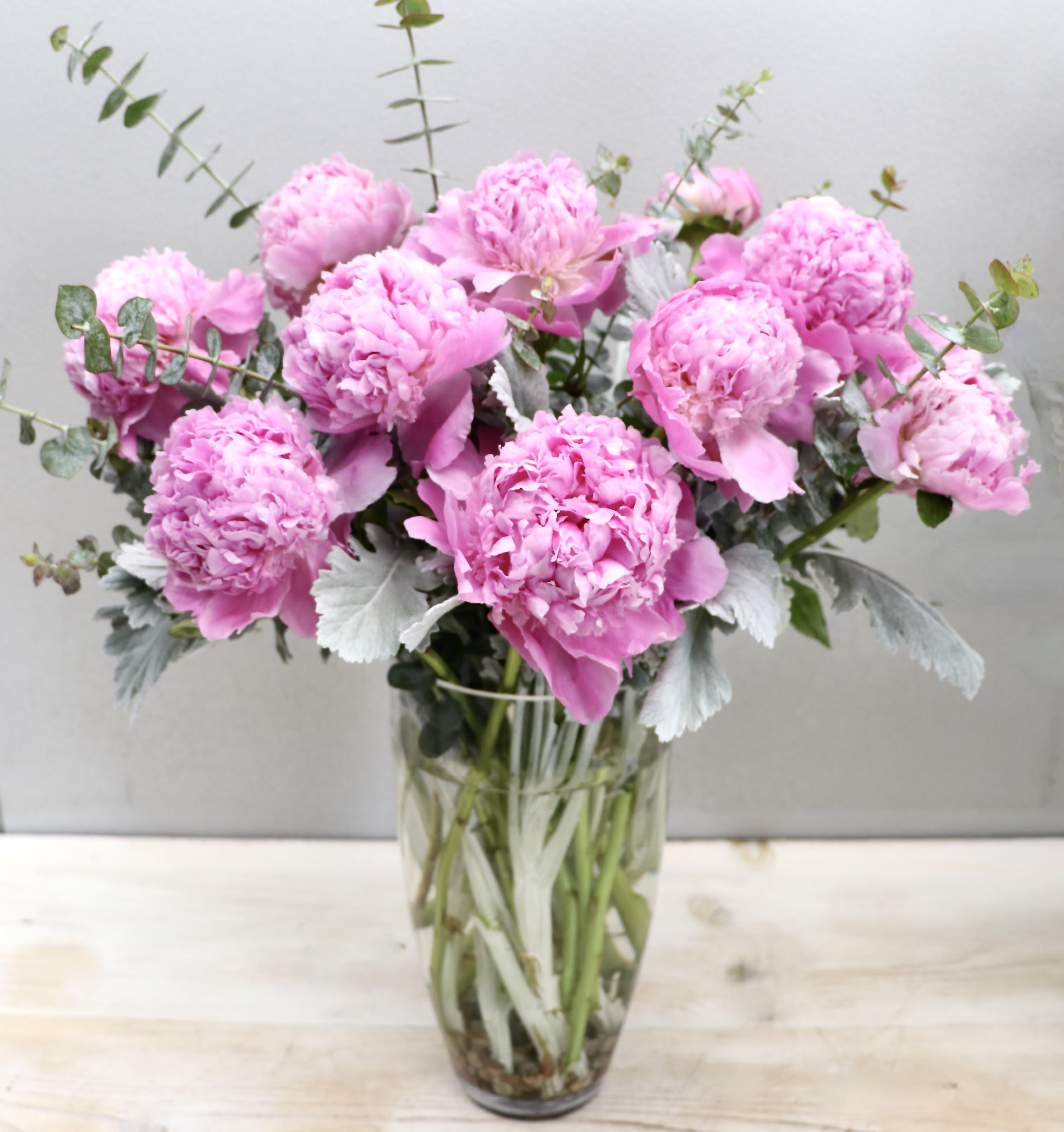 Peony Muse - Glendale Flowers - Layers of delicate pink peonies spill over the rim of a textured, tall glass vase for a look that is both timeless and tactile. This arrangement balances the airy softness of spring blooms with the clean, rhythmic lines of contemporary glasswork.