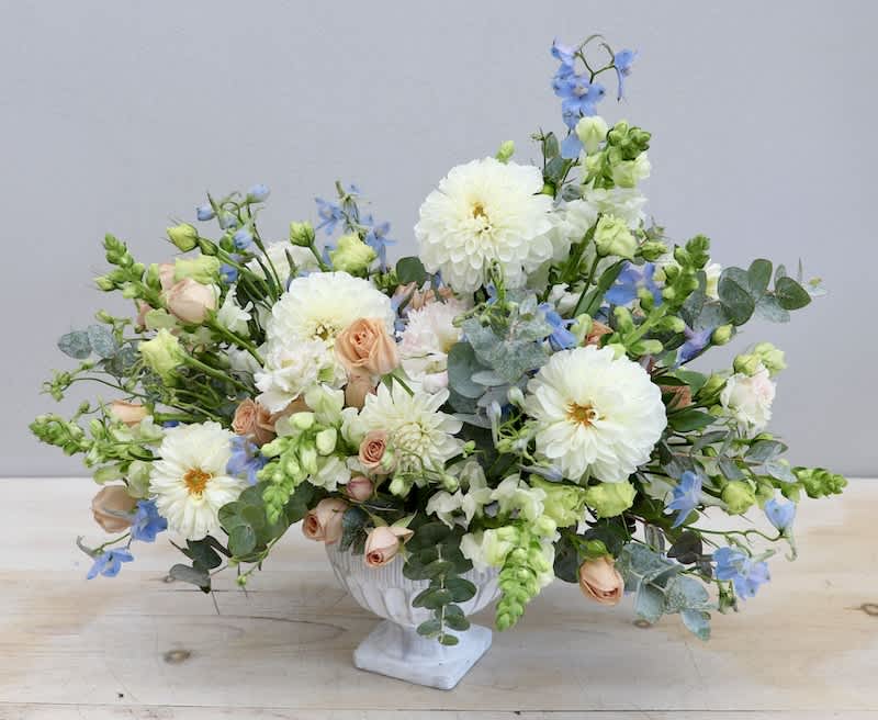 Low floral arrangement in a white pedestal vase with white, peach, and blue blooms