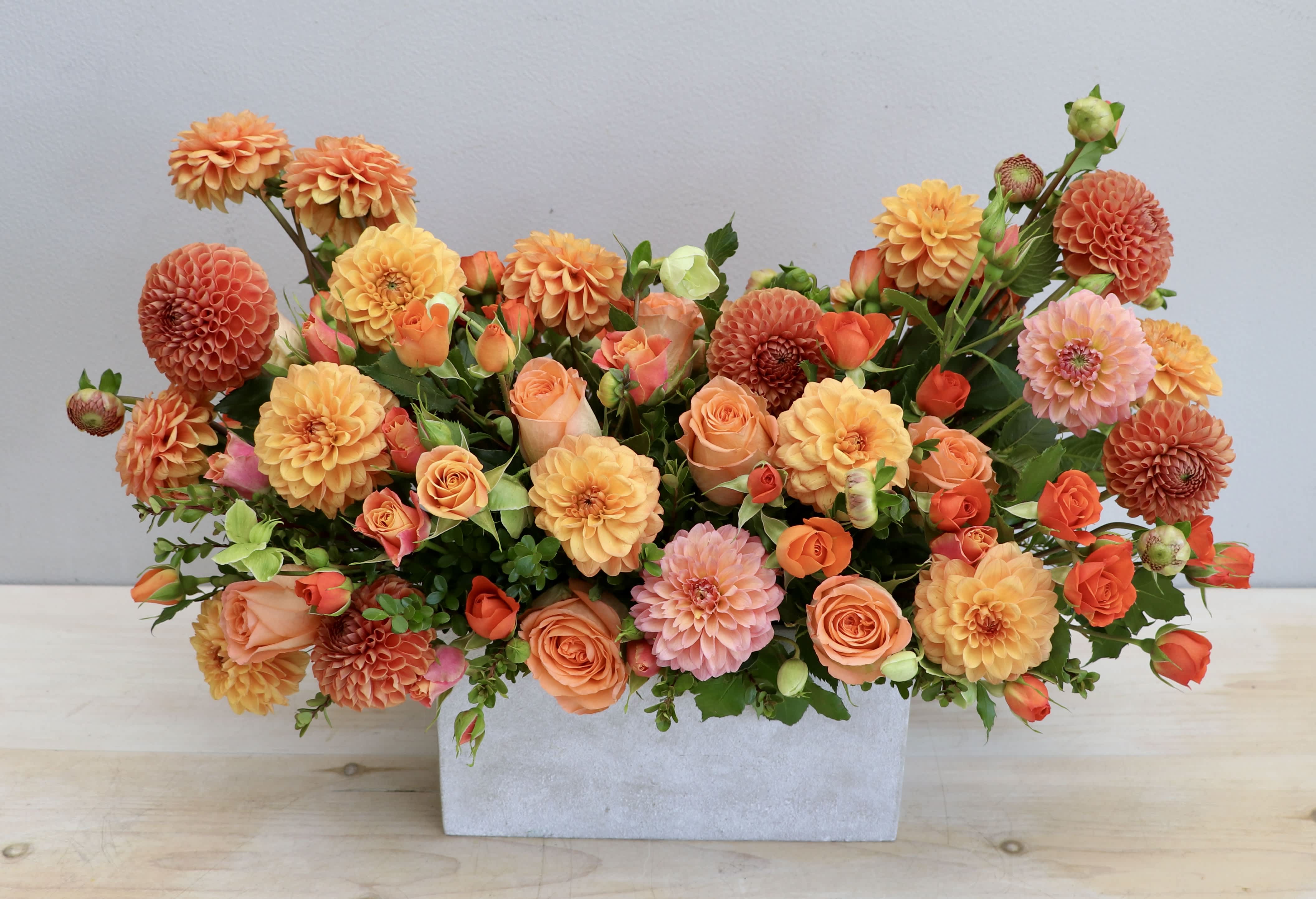 Low rectangular arrangement of orange dahlias and peach roses in a gray container