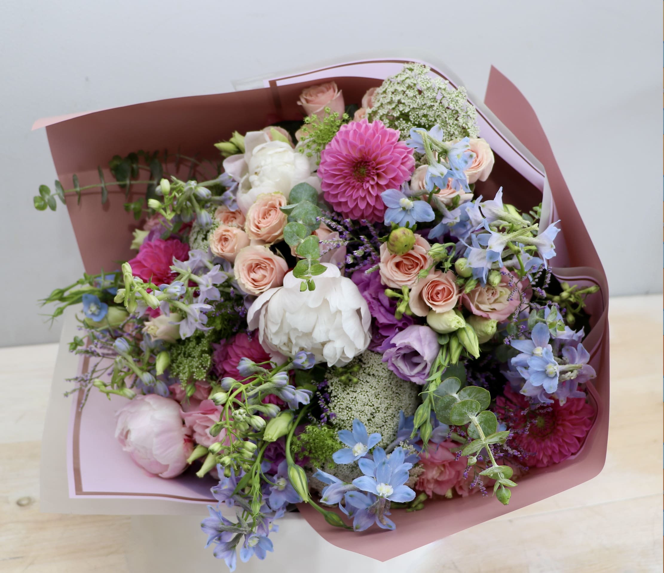 Mixed bouquet of pink, purple, blue, and white flowers wrapped in pink paper