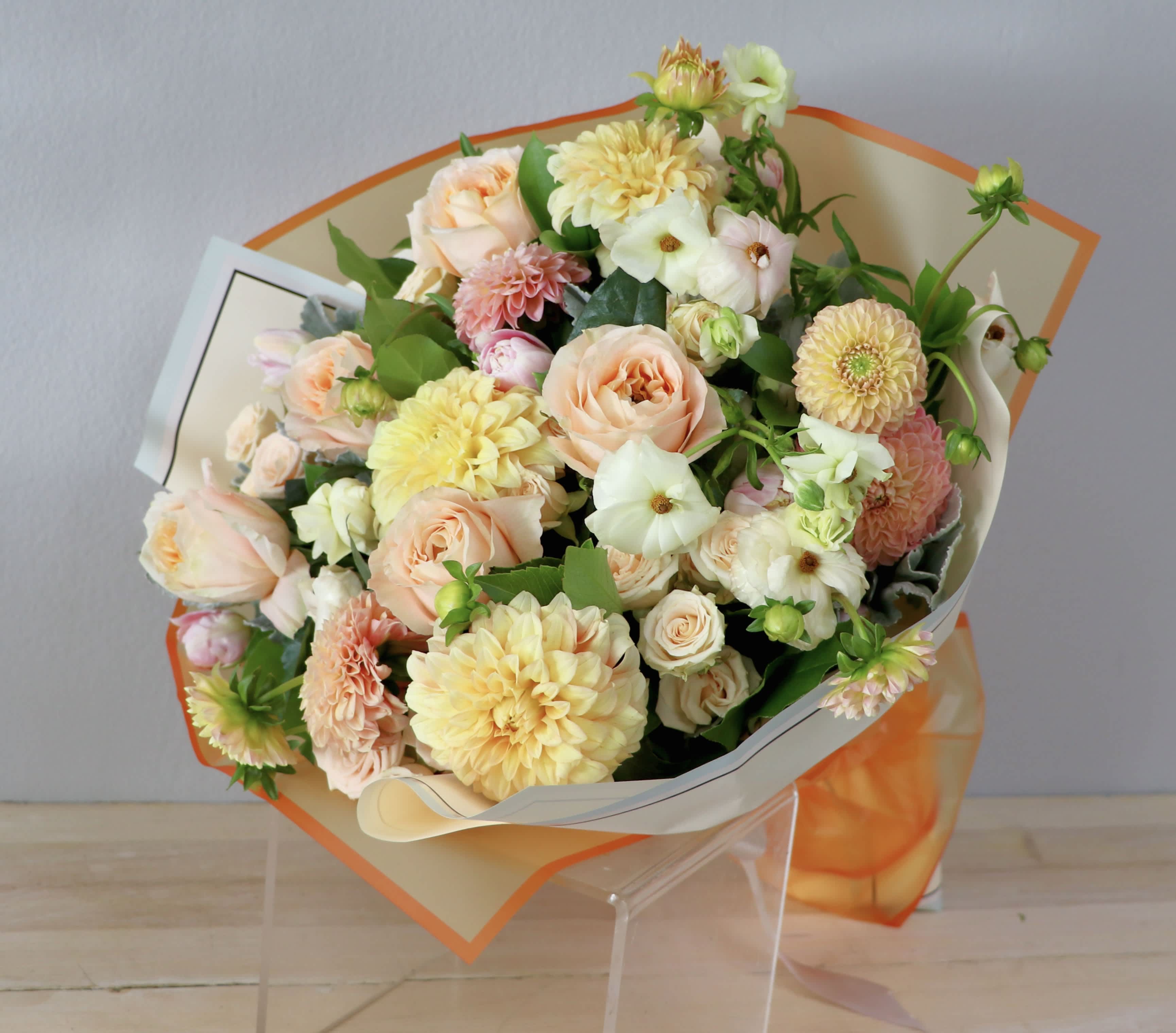 Bouquet of peach roses and pale yellow dahlias wrapped in cream and orange paper