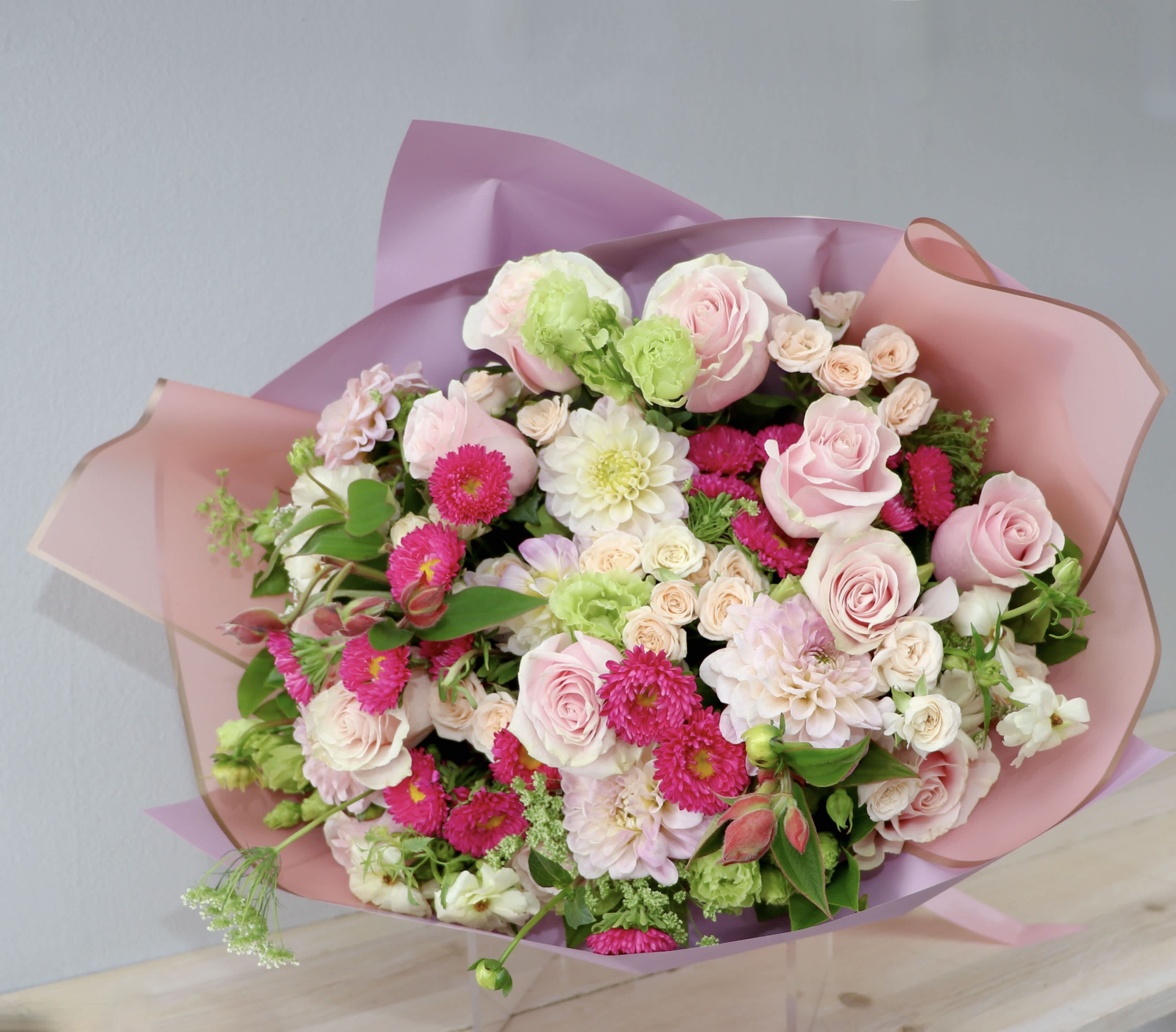 Bouquet of pink roses, white blooms, and bright pink flowers wrapped in pink paper