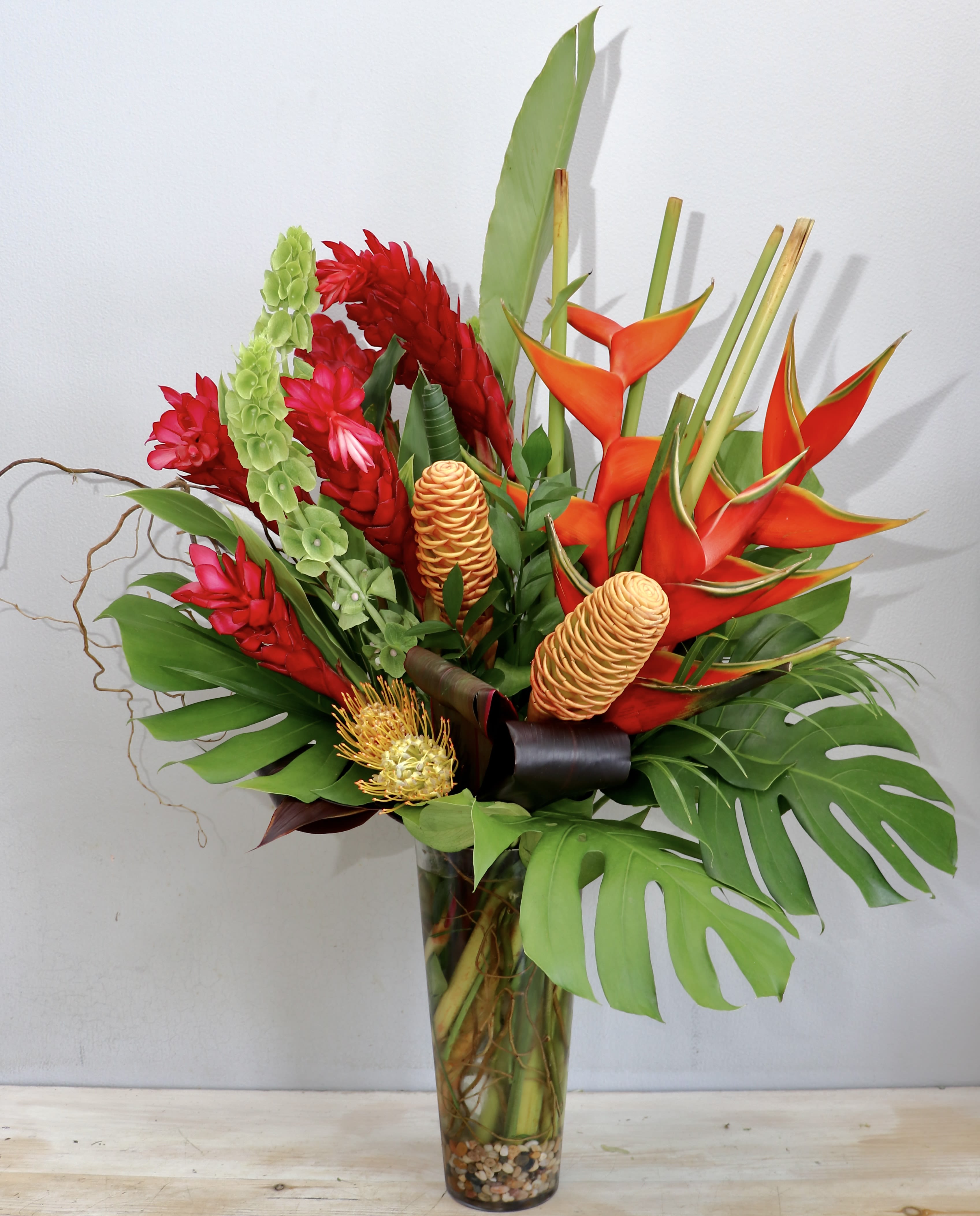 Tropical bouquet with red and orange flowers in a tall glass vase