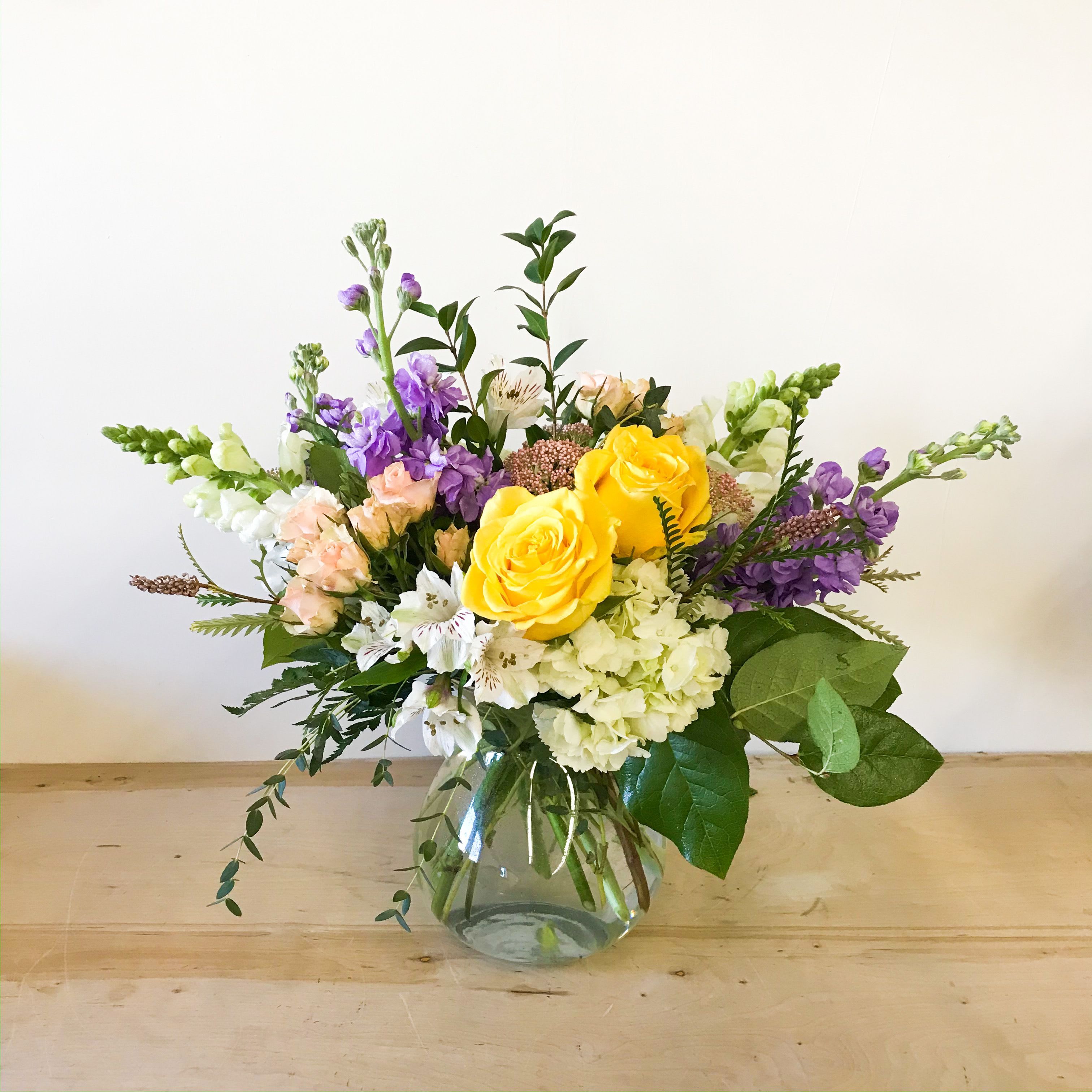 Because of You - A pastel color palette of hydrangea, roses, stock, snapdragons, alstroemeria arranged in a clear glass vase.