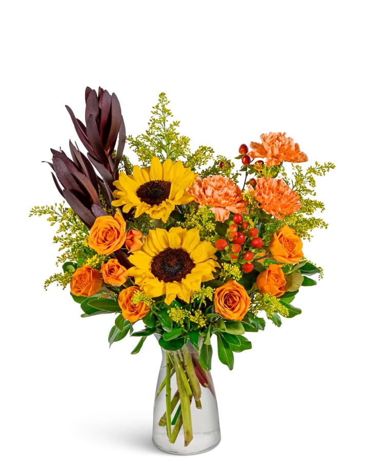 Bouquet of sunflowers, orange roses, and carnations in a clear glass vase