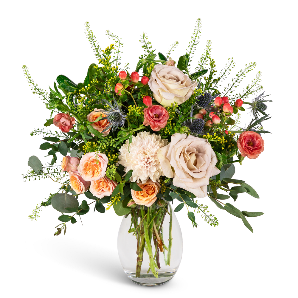 Mixed bouquet of cream, peach, and coral flowers in a clear glass vase