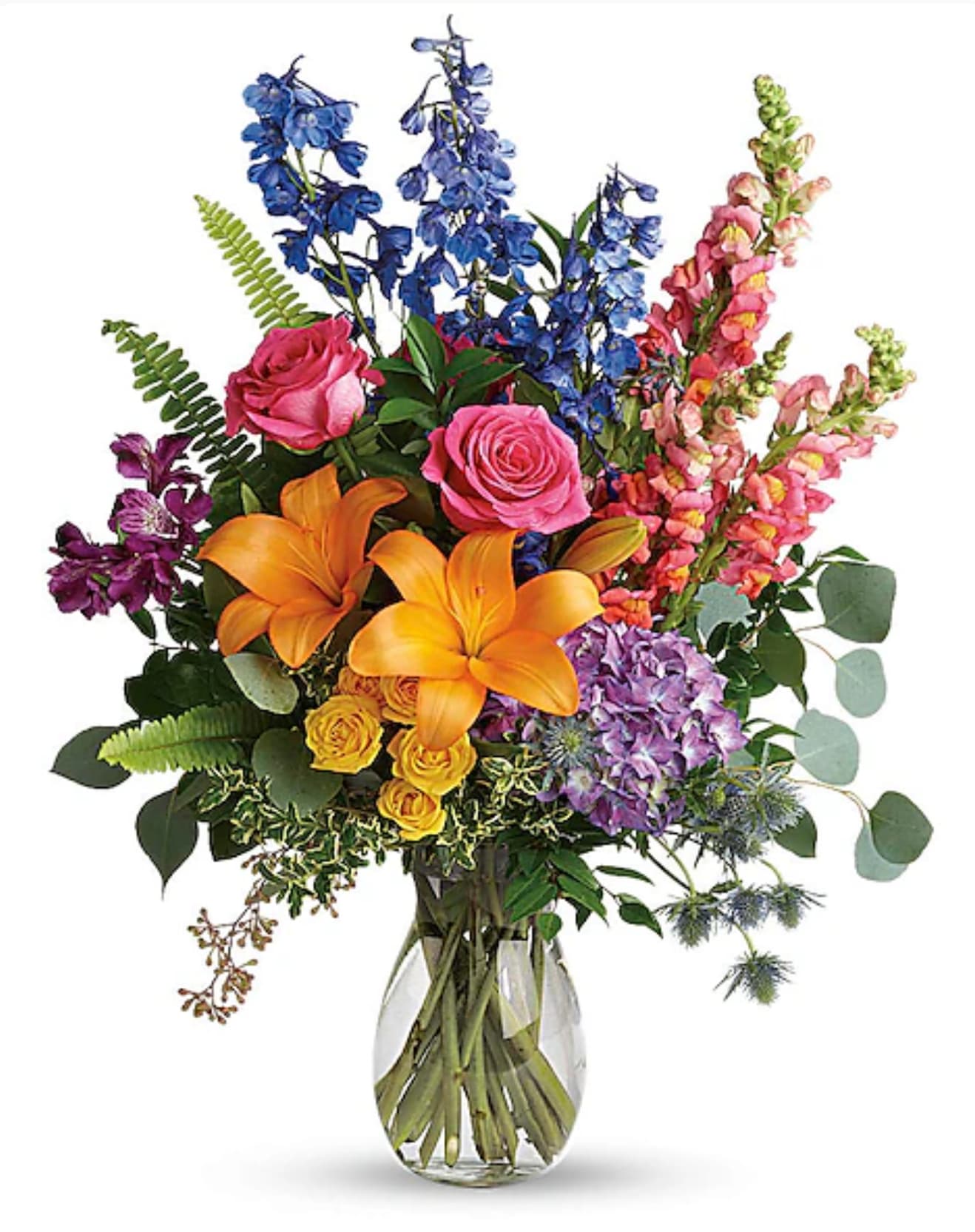 Colorful bouquet with roses, lilies, and tall blue and pink blooms in a glass vase