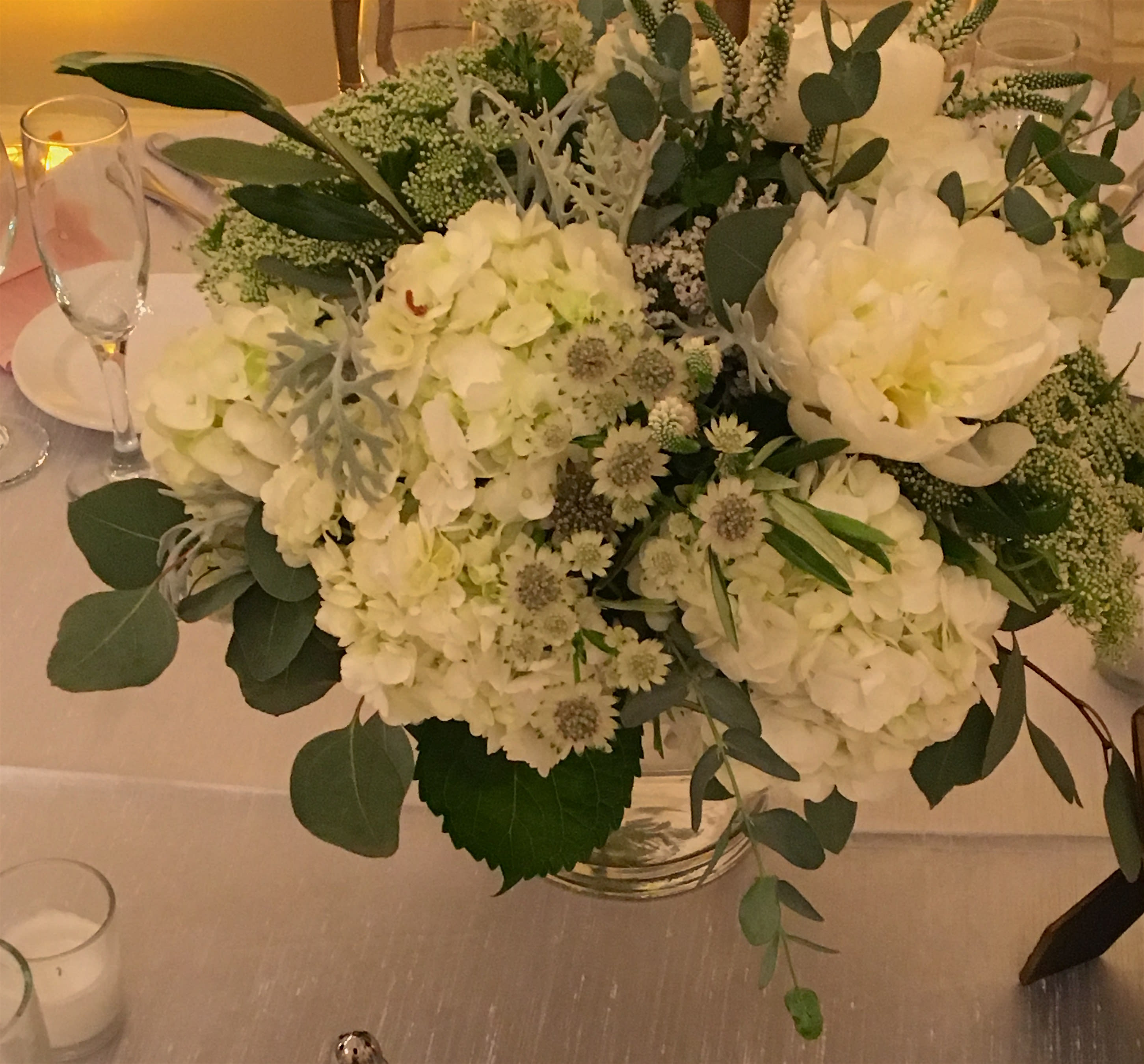 White floral centerpiece in a clear glass vase with eucalyptus