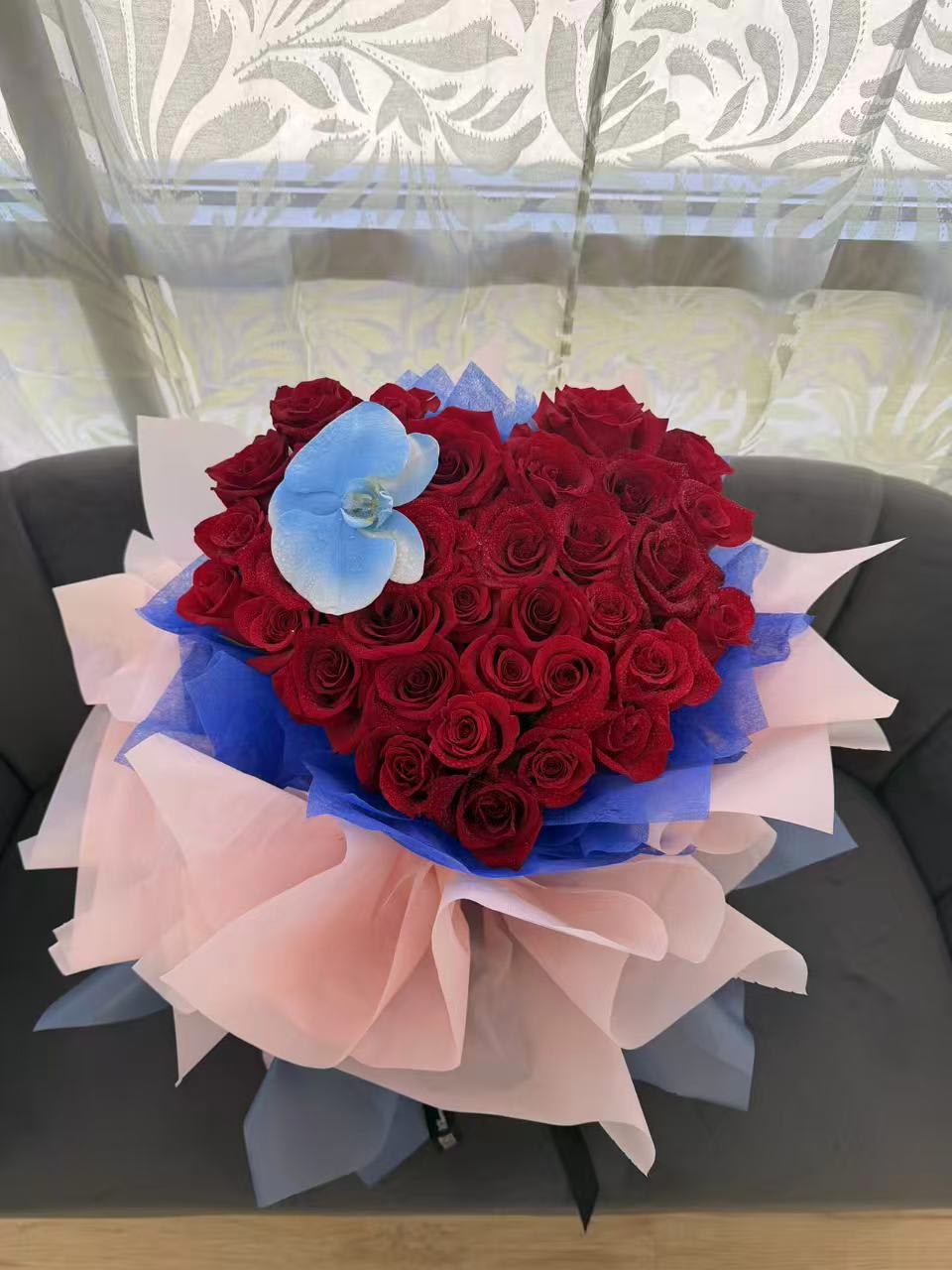 Heart-shaped bouquet of red roses with blue and pink wrapping