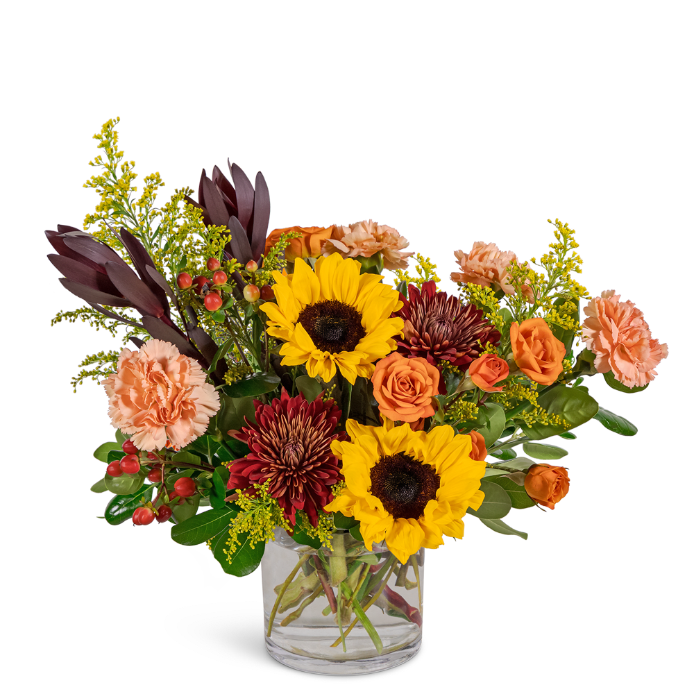 Mixed bouquet of sunflowers, roses, and carnations in a clear glass vase