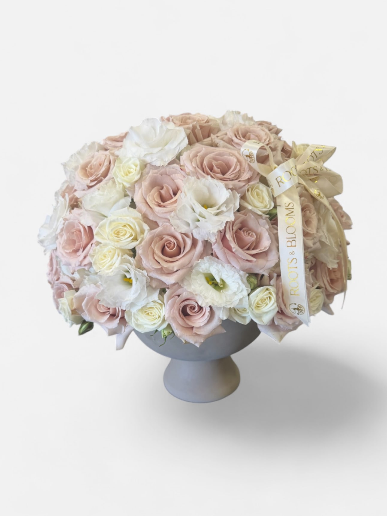 The Ivory Blush - The Ivory Blush is a luxurious garden-style arrangement featuring delicate blush roses, ivory roses, and soft white seasonal blooms. Designed in an elegant pedestal vase and finished with our signature Roots &amp; Blooms ribbon, this arrangement is perfect for birthdays, anniversaries, celebrations, or simply making someone feel special.