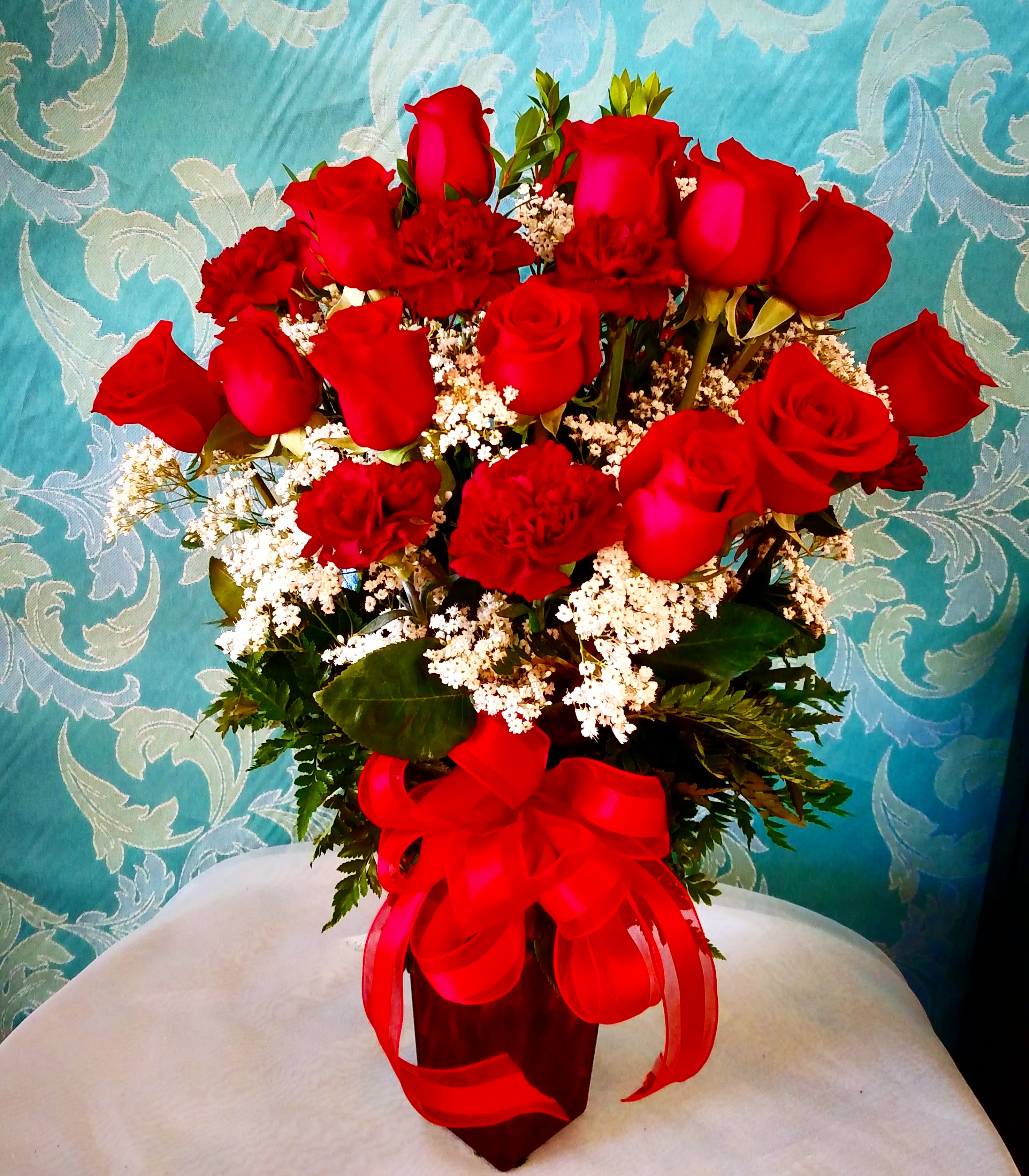 Red roses and carnations arranged in a vase with a red ribbon
