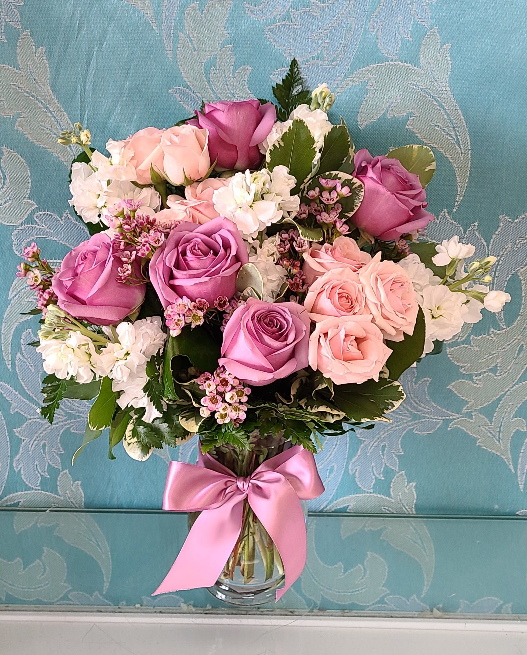 Bouquet of pink and lavender roses in a clear glass vase with a pink ribbon