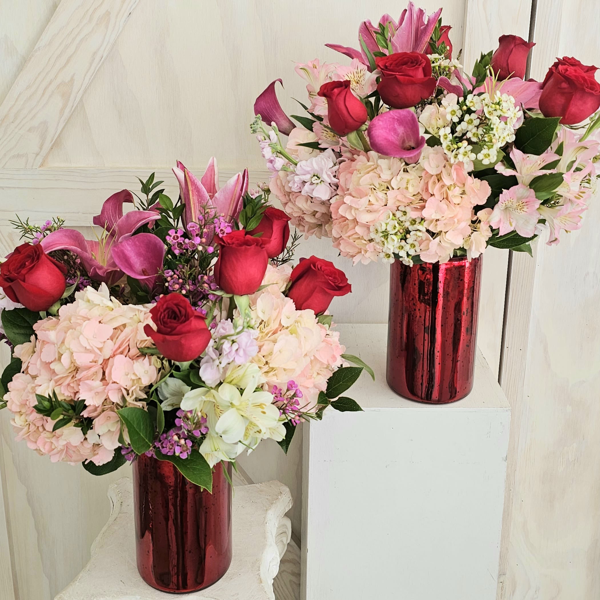 Two bouquets of red roses, pink lilies, and pale hydrangeas in red vases