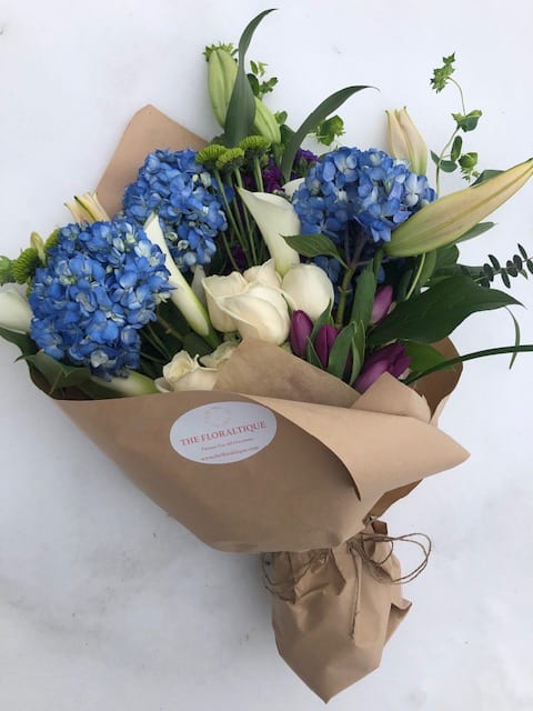 Bouquet of blue hydrangeas, white calla lilies, and purple tulips in brown paper