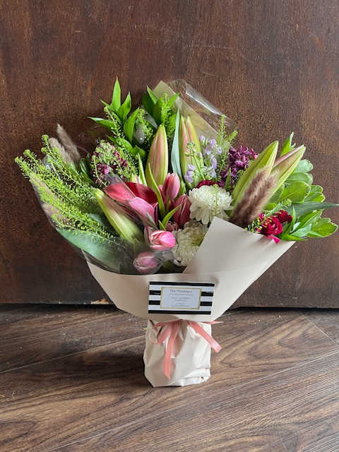 Mixed bouquet of lilies, pink blooms, and white flowers wrapped in paper