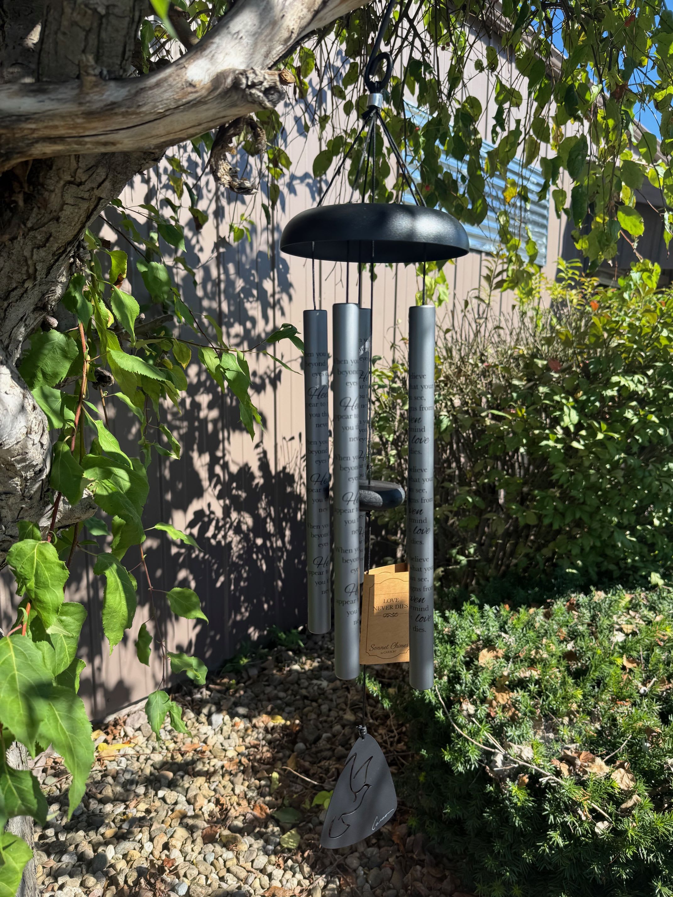 Black memorial wind chime hanging outdoors among trees and shrubs