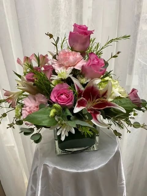 Pink roses and lilies arranged in a square glass vase