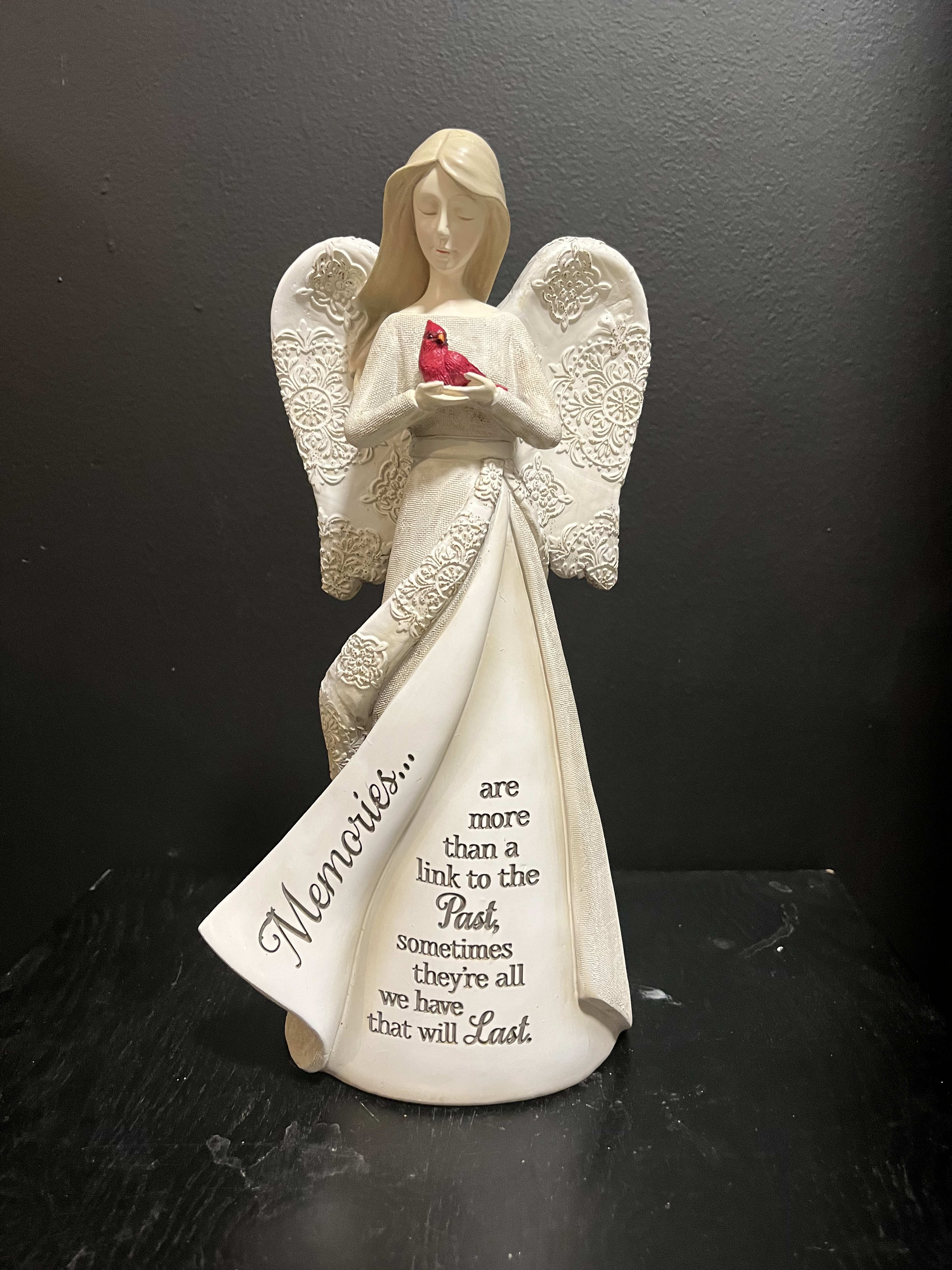 White angel figurine holding a red bird with a memorial message on the robe