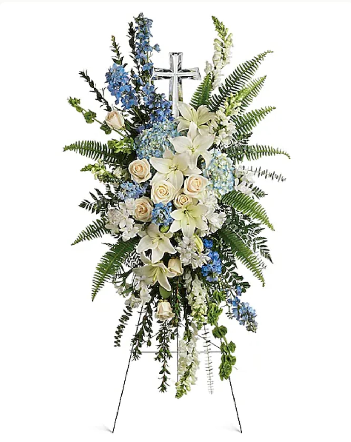 Standing floral spray with white lilies, cream roses, and blue flowers on an easel cross