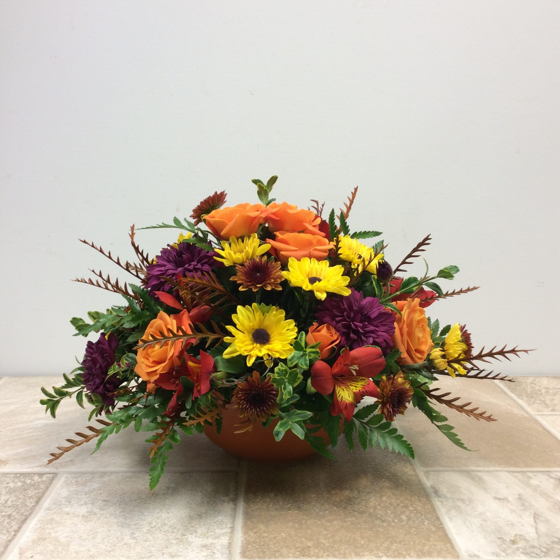 Low floral arrangement with orange roses, yellow daisies, and purple blooms in a bowl vase